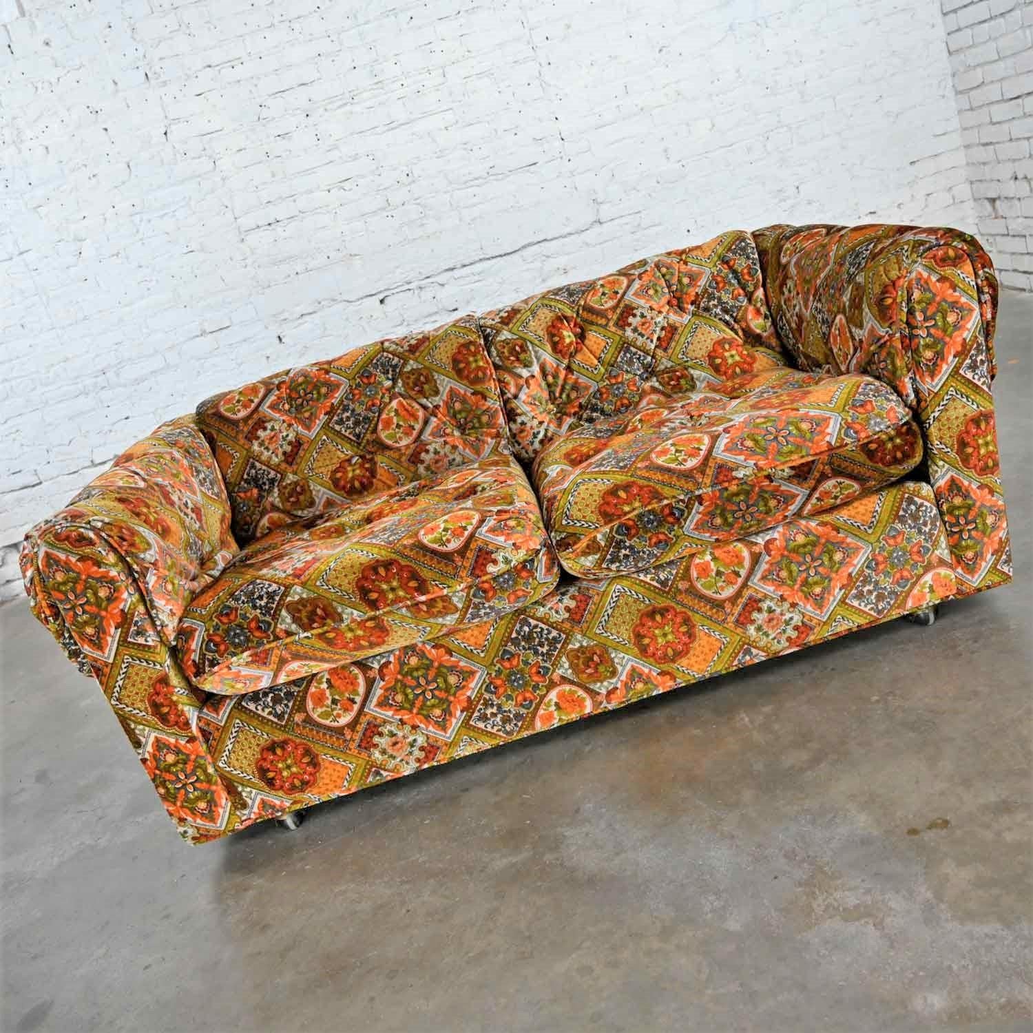 Beautiful vintage modern tuxedo style love seat with original orange & gold geometrical or floral patchwork velvet like fabric and semi attached extra padded button tuck arms and back. It is labeled Maddox Furniture for J.C. Penney 5/30/1979. Lovely
