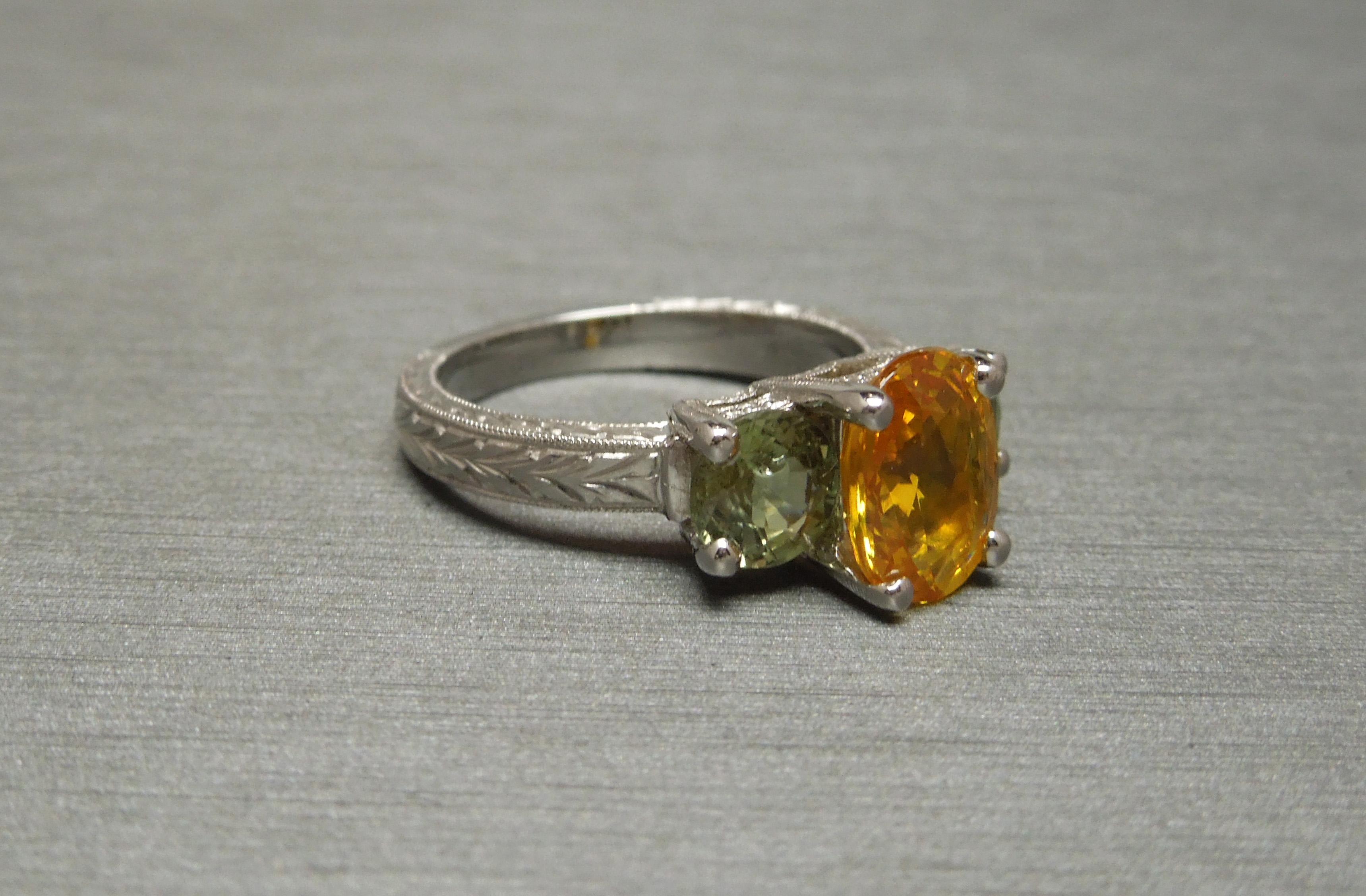 This Orange & Green Sapphire Three-Stone Ring features 3 Pastel-shade Natural Sapphires in the two most prominent earth tones: a Golden Orange & an Earthy Green, representing the Sun & Earth. Central Oval cut weighing 2.65 carats at 8.3mm x 6.1mm &