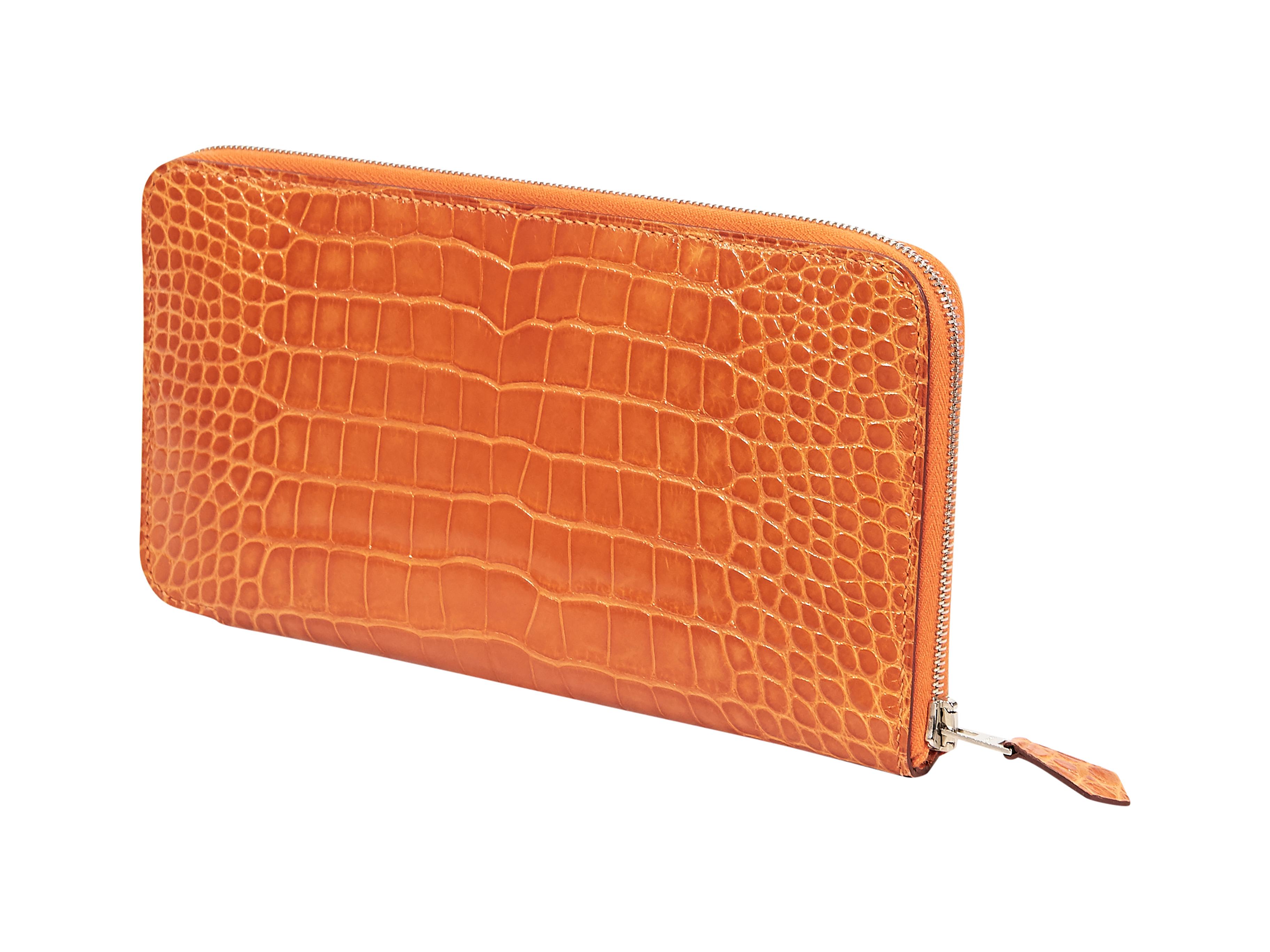 Product details:  Orange alligator wallet by Hermes.  Zip-around closure.  Leather interior with multiple inner credit card slots and center zip coin pouch.  Silvertone hardware.  Dust bag included.  7.75