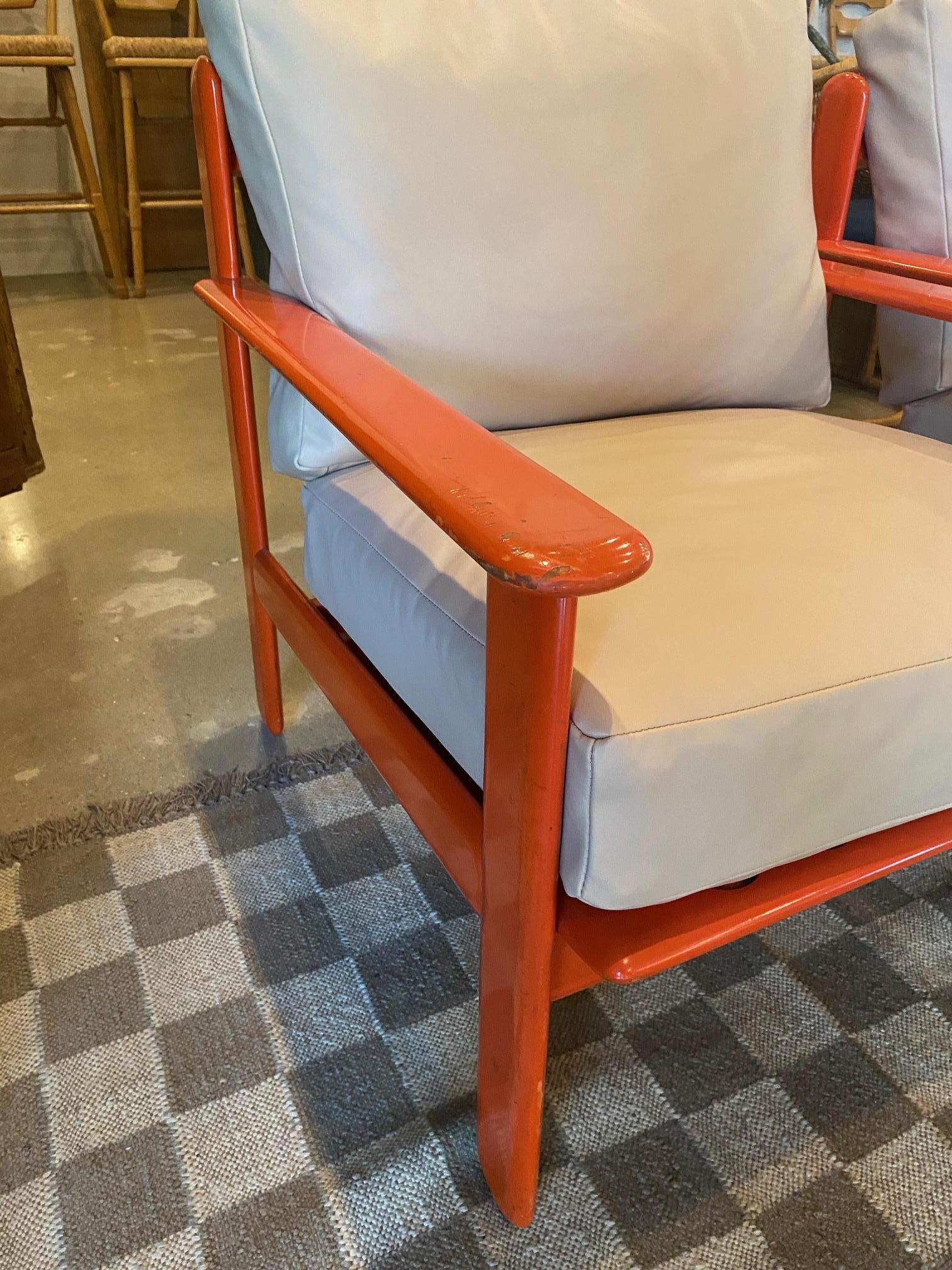 Pair orange lacquered open frame armchairs with new buff leather cushions.  Reddish-orange finish on solid hardwood thin profile frames are paired with loose leather seat and back cushions that have zippers and down wrapped foam inserts. 