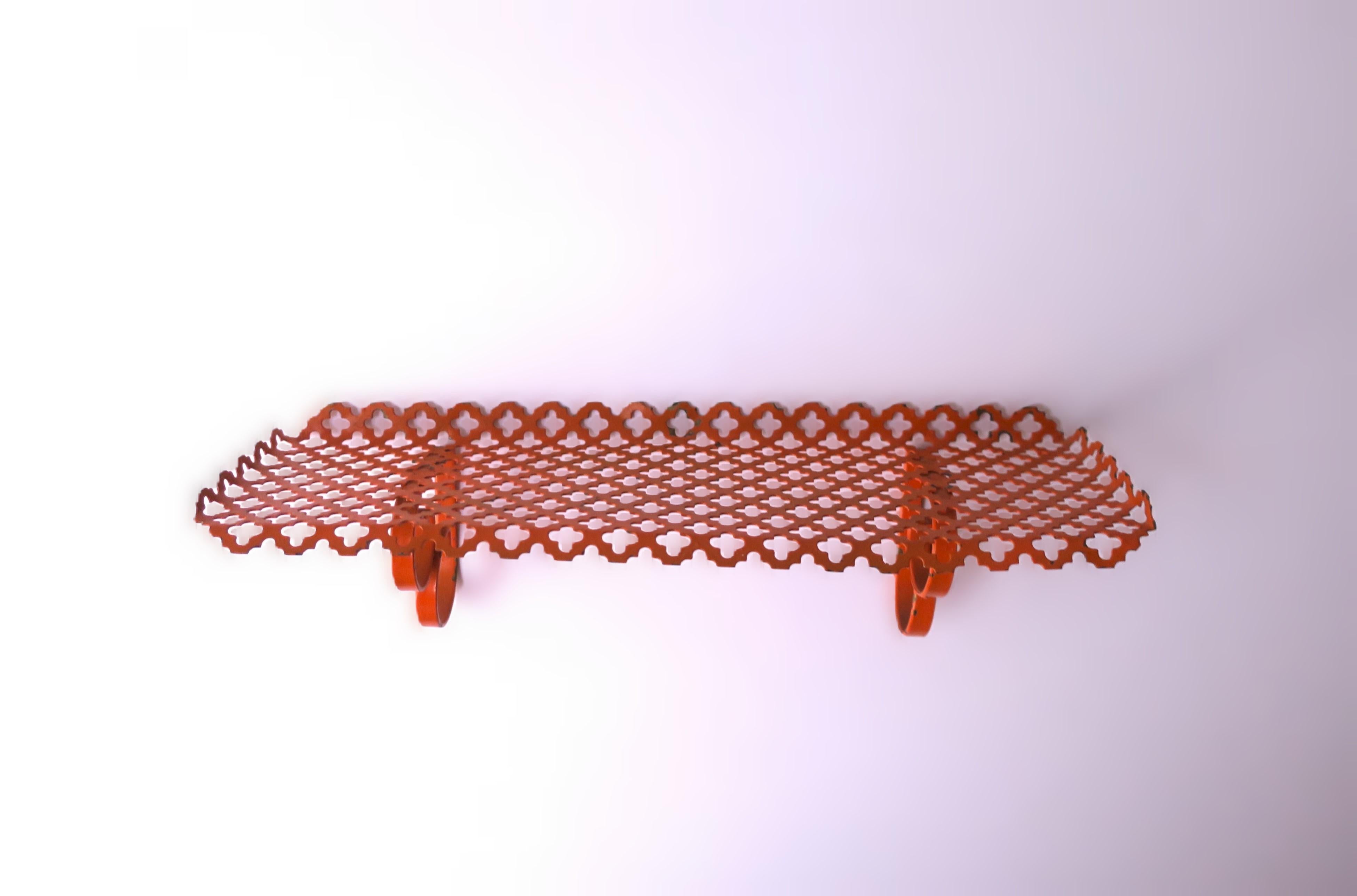 An orange metal wall shelf with perforated design, circa mid-20th century, 1960s. Piece may work well in a bedroom, bathroom, kitchen, etc., to hold various items (demonstrated holding perfume bottles.) Dimensions: 4.63