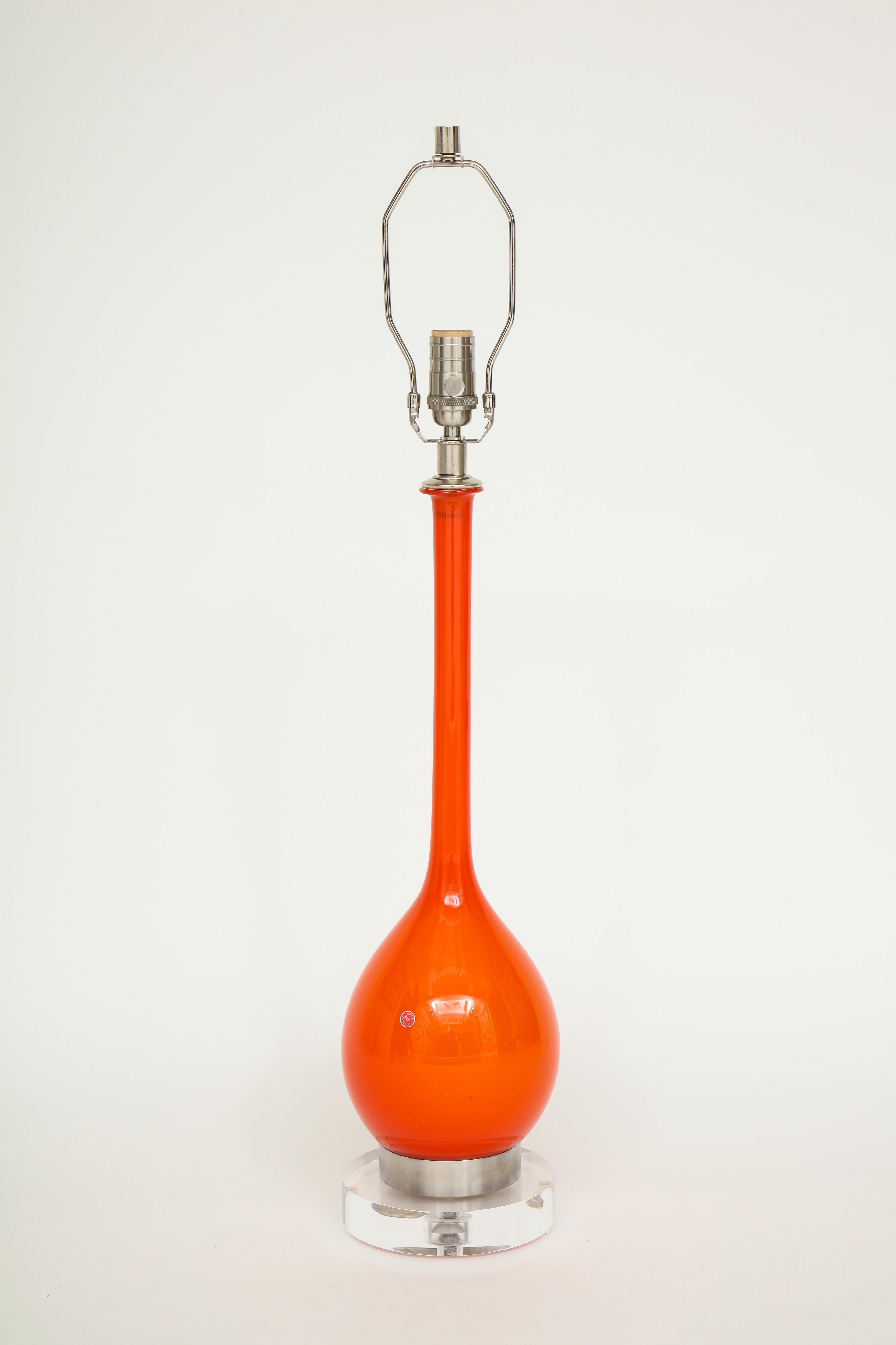 Vibrant orange Murano glass lamps with elongated necks and orb bodies mounted on nickel bands and lucite bases. Rewired for use in the USA. 100 W bulb max. Base and glass body measures 23.25 inches.