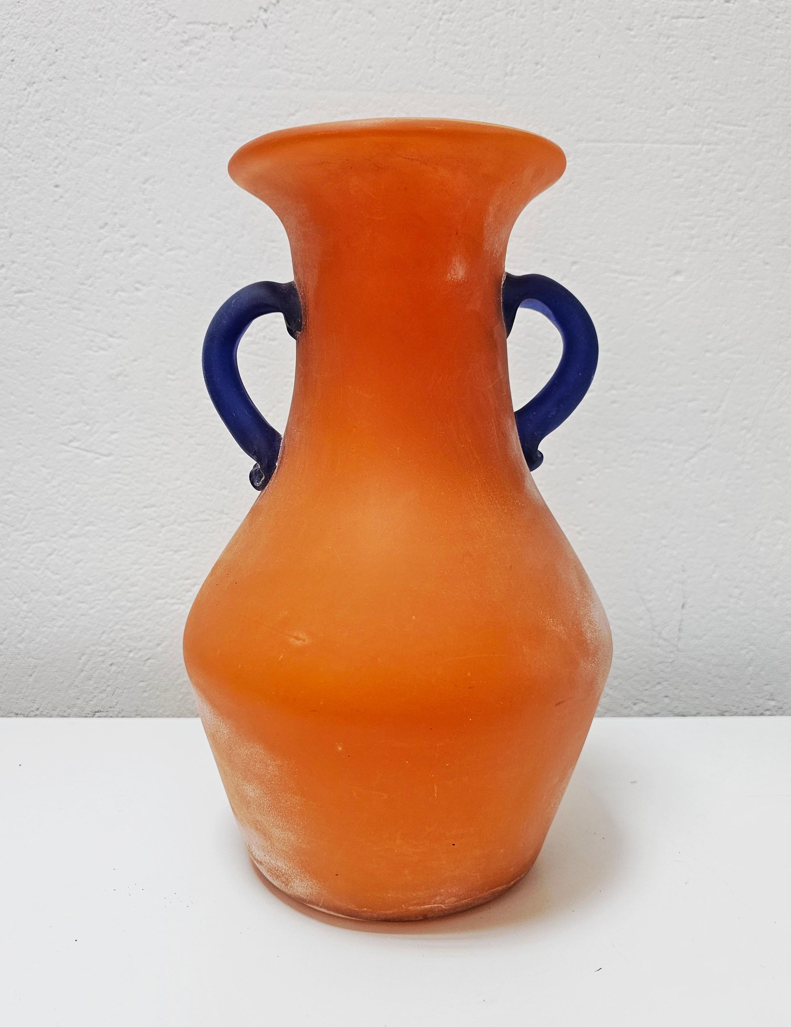 Vous trouverez dans cette annonce un superbe et rare vase Scavo en verre de Murano de très grande taille, réalisé en verre orange vibrant, avec les anses en verre bleu profond. Le vase a été conçu par Carlo Moretti dans les années 1970 dans