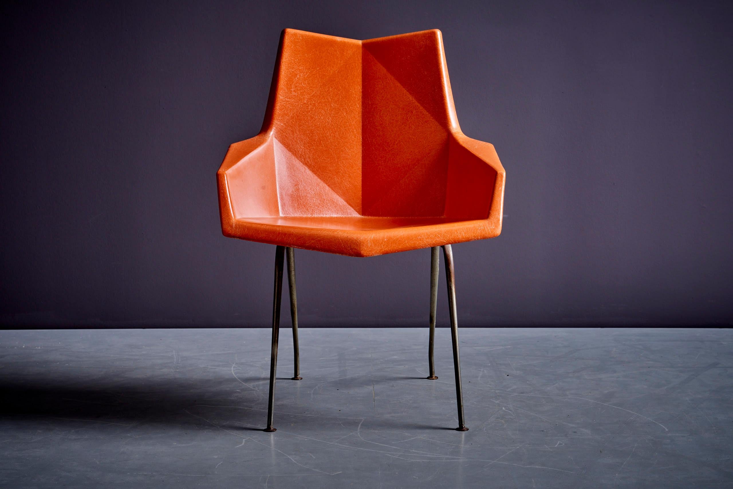 Una silla de origami Paul McCobb naranja de los años 50 para asientos St. John. El asiento de fibra de vidrio está moldeado en ángulos, lo que recuerda la técnica japonesa del origami. La silla se alza sobre una rara base angulada de hierro macizo.