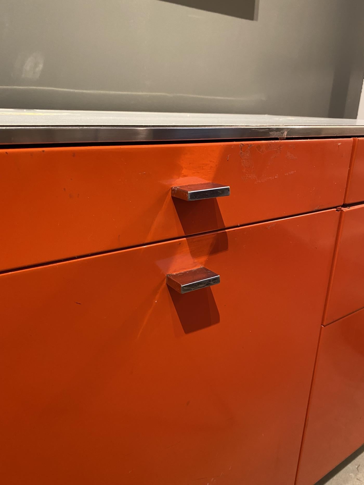 Industrial credenza in bright orange by Davis Allen for GoodForm. White laminate top, shop-painted metal in orange, and polished stainless steel drawer pulls and legs. Four shallow drawers, two deeper drawers, two file drawers, and two hinged
