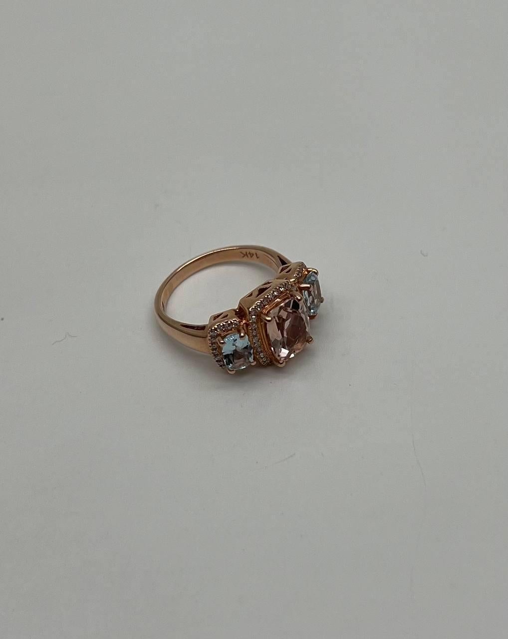 Dieser exquisite Ring besteht aus einem warm getönten Band aus 14 Karat Roségold. In der Mitte befindet sich ein atemberaubender rechteckiger pfirsichfarbener Morganit, flankiert von zwei kleineren blauen Aquamarinen auf jeder Seite. Die Fassung ist