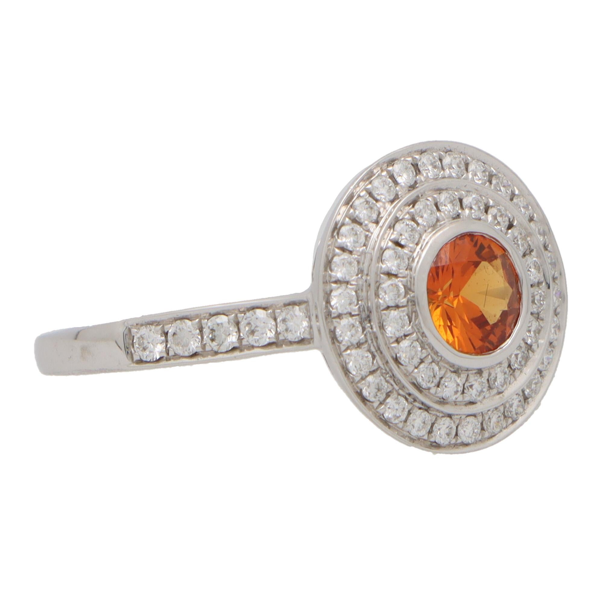A beautiful orange sapphire and diamond double target ring set in 18k white gold.

The ring is predominantly set with a sparkly round cut orange sapphire which is bezel set securely to centre. Surrounding this beautiful diamond are two targets of