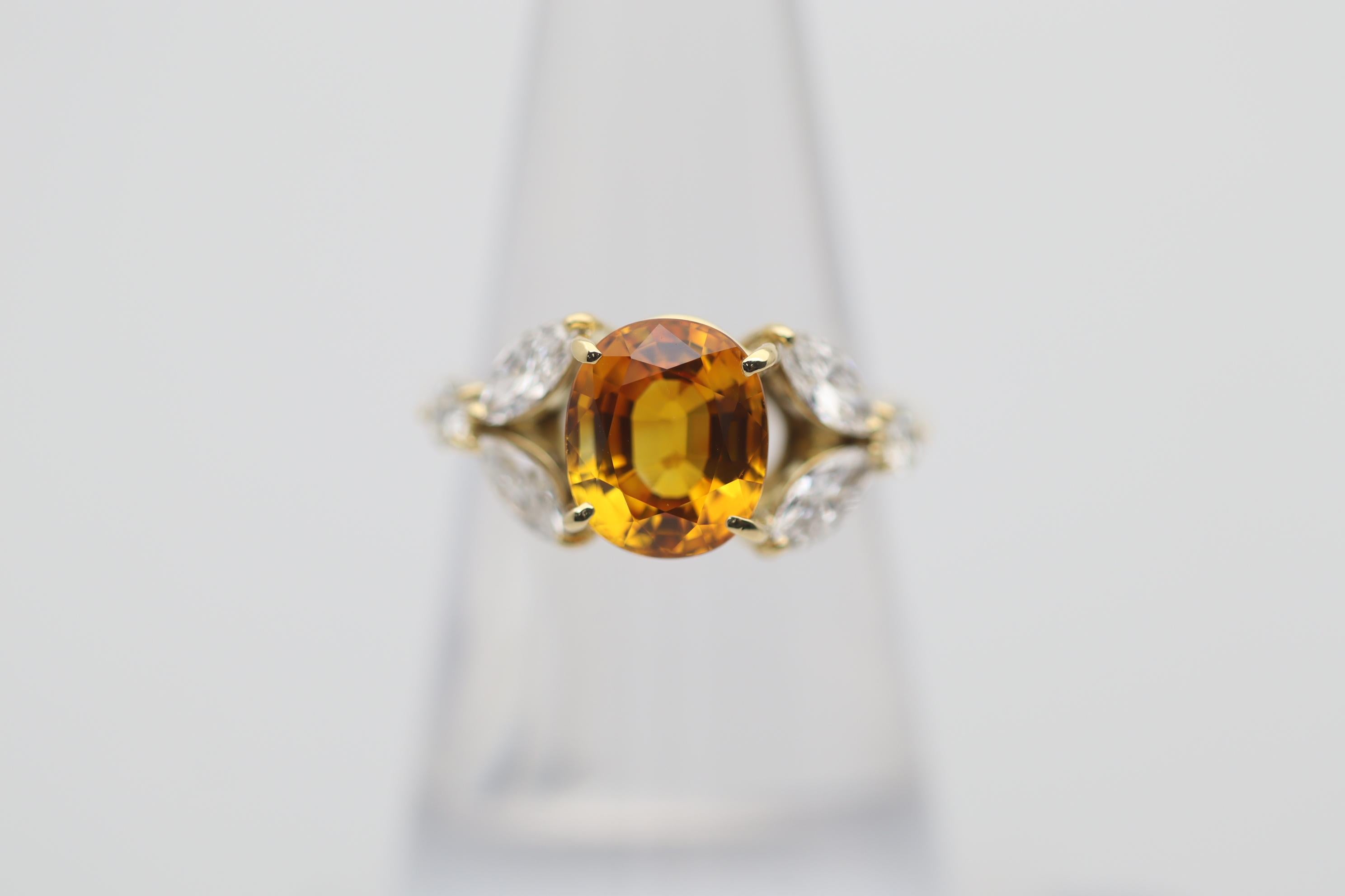 A sweet and stylish ring featuring a bright vivid orange sapphire weighing 3.58 carats. It has a rich orange color and a lovely oval shape. Complementing the sapphire are 0.81 carats of large marquise and round brilliant-cut diamonds set in a floral