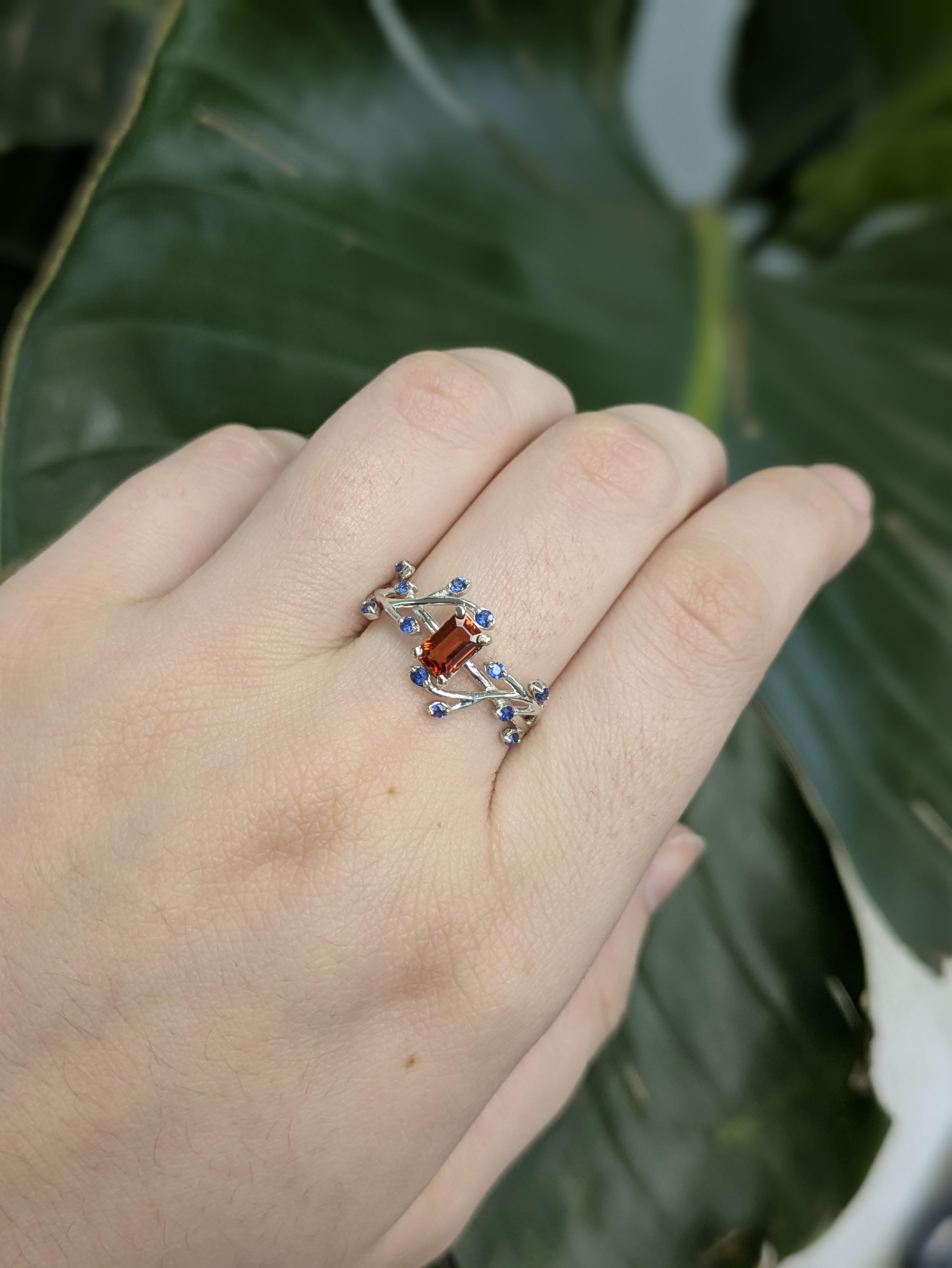 This timeless ring features a 0.71ct emerald-cut heated Orange sapphire at its center, measuring 6x4mm. Crafted in 14K gold (2.2g), it’s accented with a secondary blue sapphire, adding extra depth and brilliance. A refined and classic piece perfect