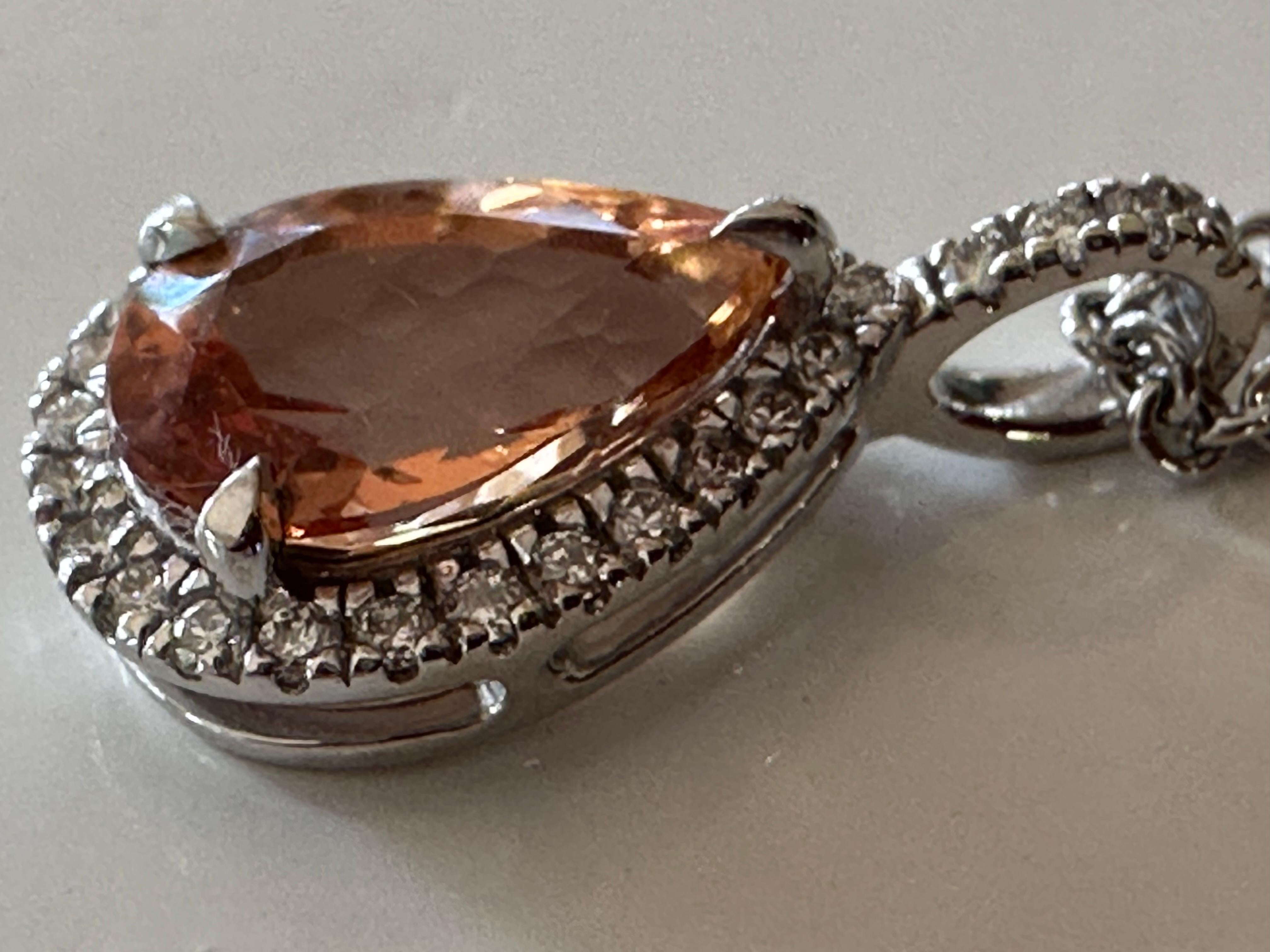Handcrafted in 14K white gold, this exquisite pendant necklace features a 2.94-carat pear-shaped orange topaz surrounded by a halo of twenty-eight round diamonds, G color, SI1 clarity totaling 0.24 carats. 
