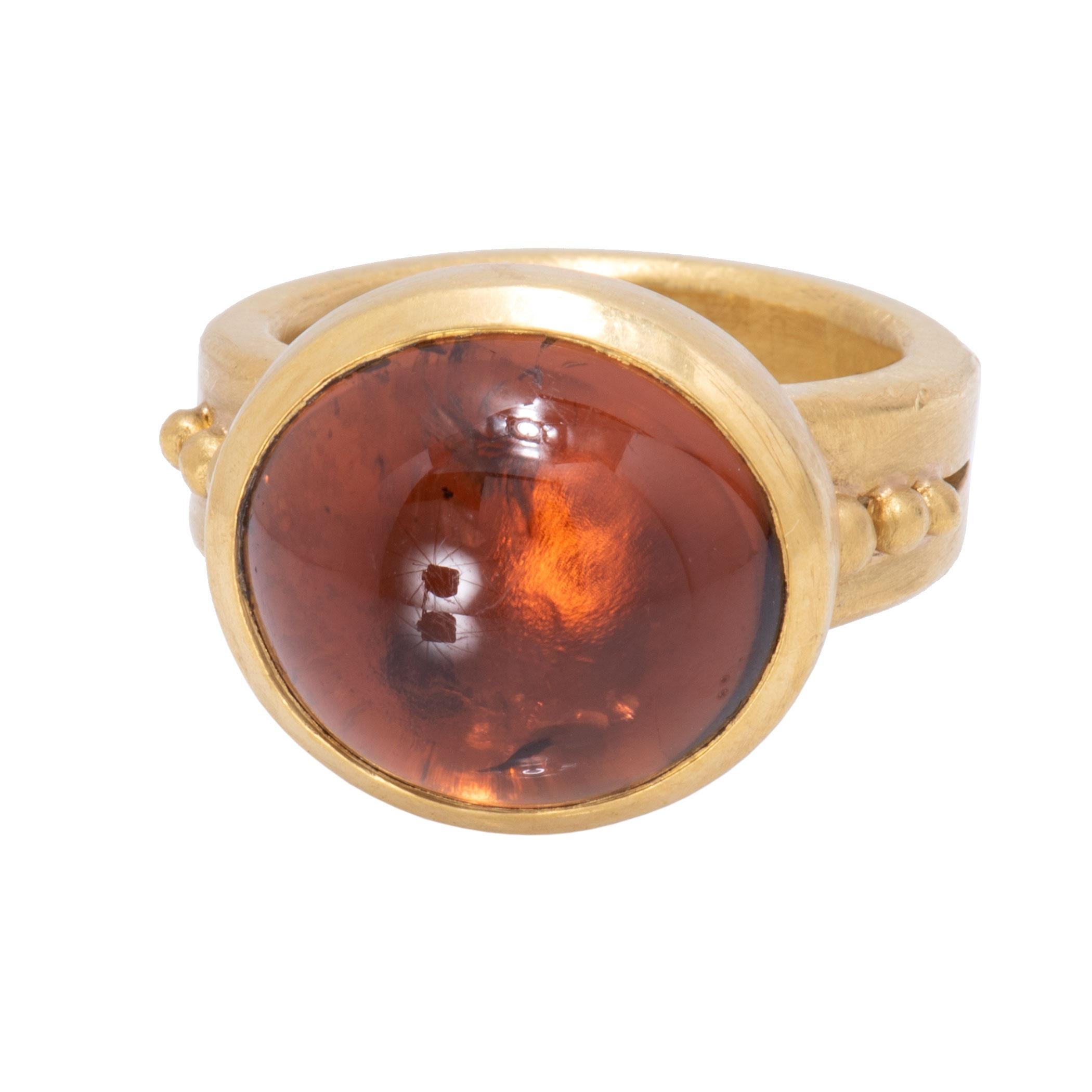 A stunning orange tourmaline cabochon 13.1 carats is bezel set high and wide in this 22 karat gold ring. A fire of lights is reflected from the depths in golds, rust, yellow and deep orange as it turns on the hand. Mounted on a wide, solid band, the