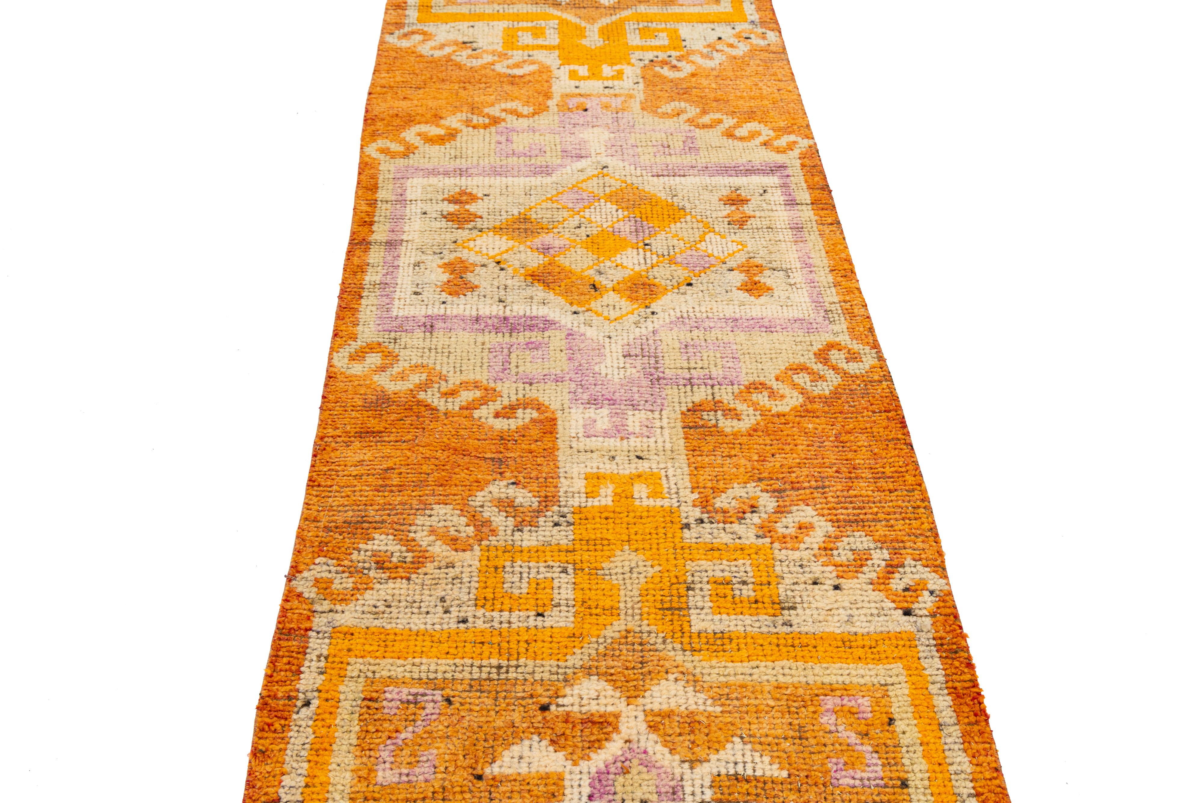 Tejido a mano en Turquía, este tapete Vintage presenta tres atrevidos medallones en forma de diamante enmarcados por motivos tribales escalonados en tonos cálidos de naranja, marfil y lavanda. Inspirado en los diseños kilim vintage, su disposición
