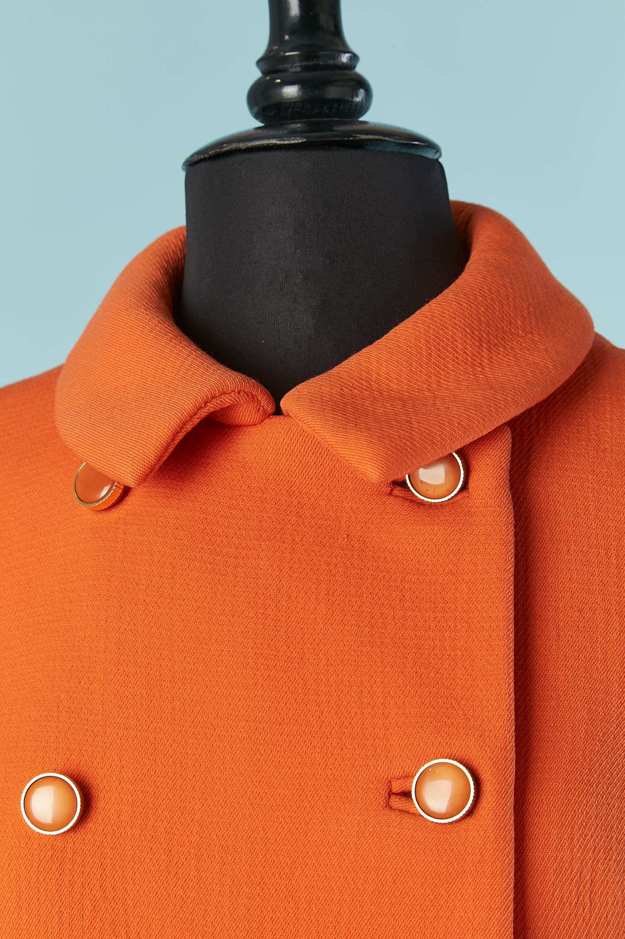 Cappotto doppiopetto in lana arancione . La fodera è probabilmente in acetato o rayon. 
Chiusura con bottoni, asole e bottoni automatici sul davanti. 
TAGLIA M