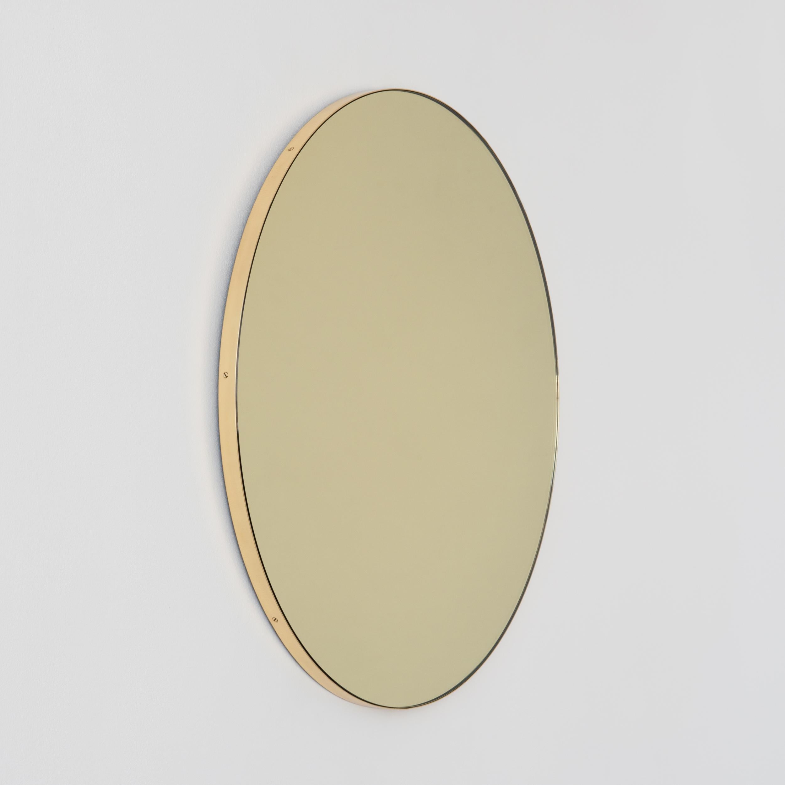 Contemporary gold tinted Orbis™ round mirror with a minimalist solid brushed brass frame. The detailing and finish, including visible brass screws, emphasise the craft and quality feel of the mirror, a true signature of our brand.  Designed and made