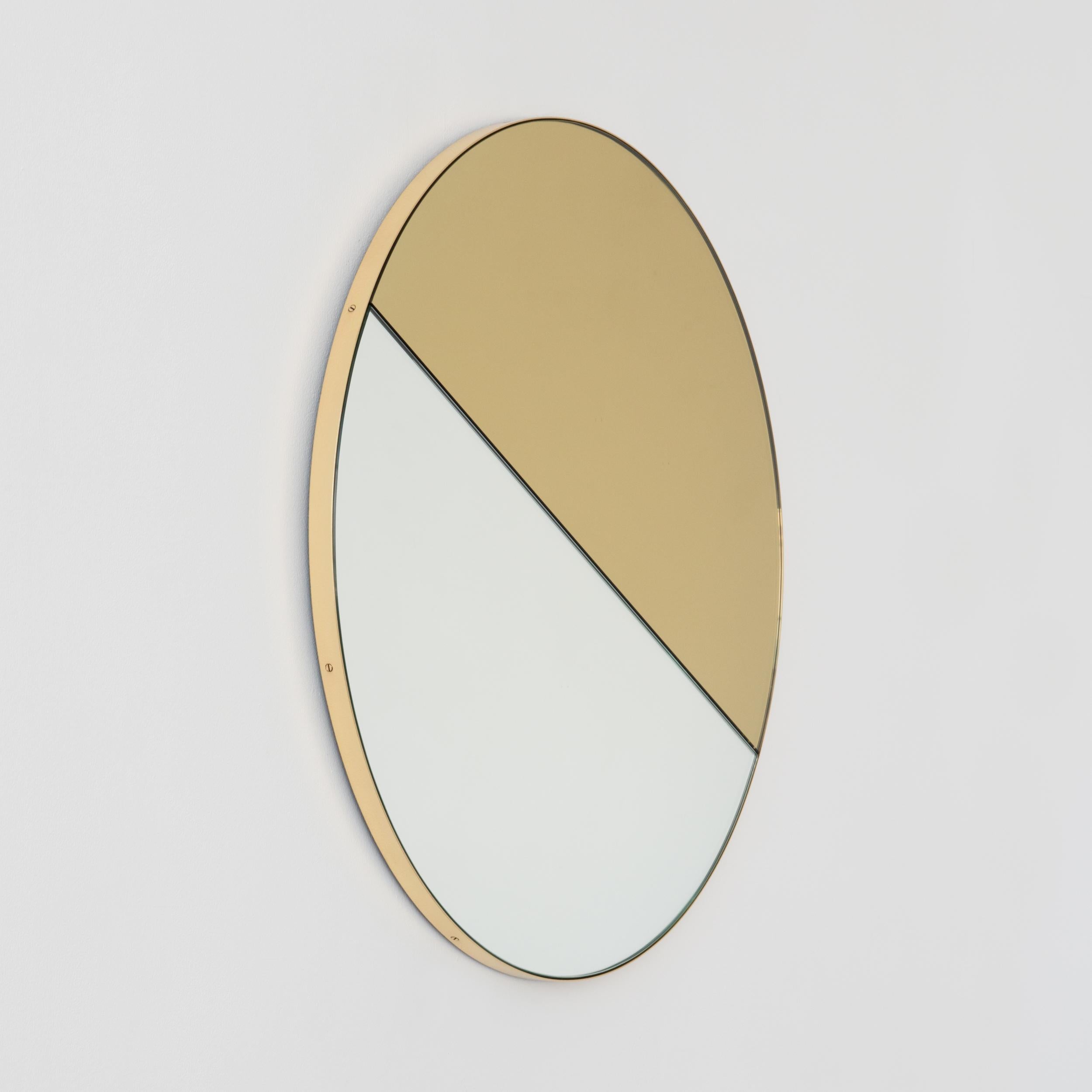 Miroir contemporain teinté mixte or et argent Orbis Dualis™ avec un élégant cadre en laiton massif brossé. Livré entièrement équipé d'un système d'accrochage spécialisé qui permet de suspendre le miroir dans quatre positions différentes. Conçu et