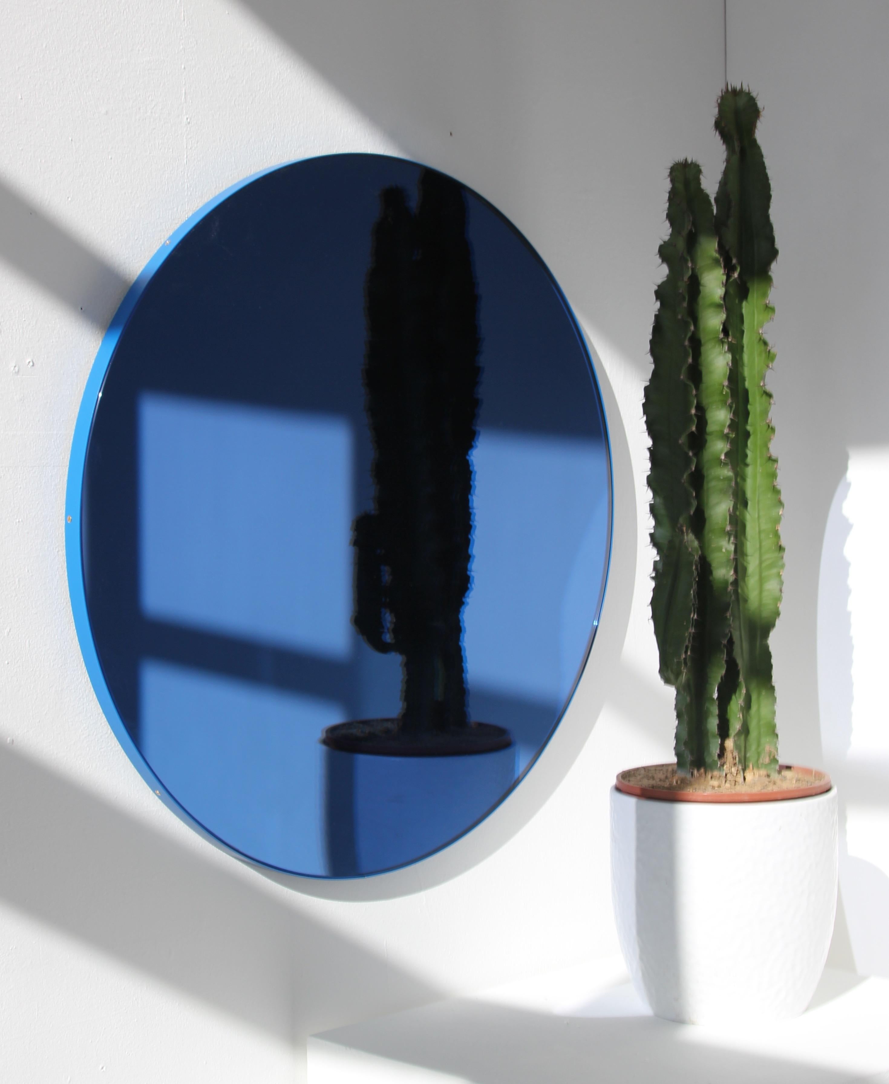 Zeitgenössischer, blau getönter, runder Spiegel mit einem blauen, pulverbeschichteten Aluminiumrahmen. Entworfen und handgefertigt in London, UK.

Die mittelgroßen, großen und extragroßen Spiegel (60, 80 und 100 cm) sind mit einem ausgeklügelten