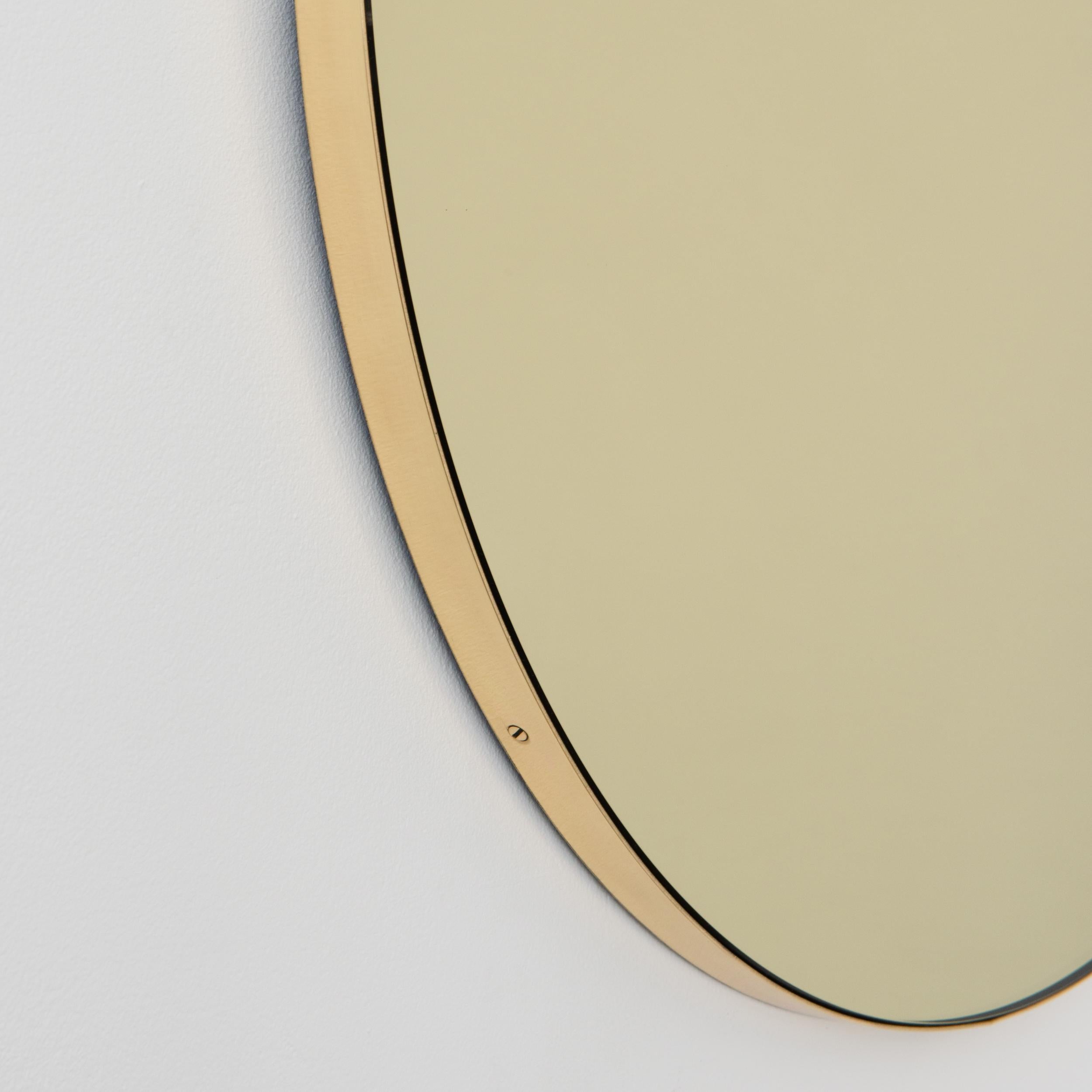 Miroir rond Orbis™ contemporain teinté d'or avec un cadre minimaliste en laiton brossé massif. Les détails et la finition, y compris les vis en laiton visibles, soulignent l'aspect artisanal et la qualité du miroir, véritable signature de notre