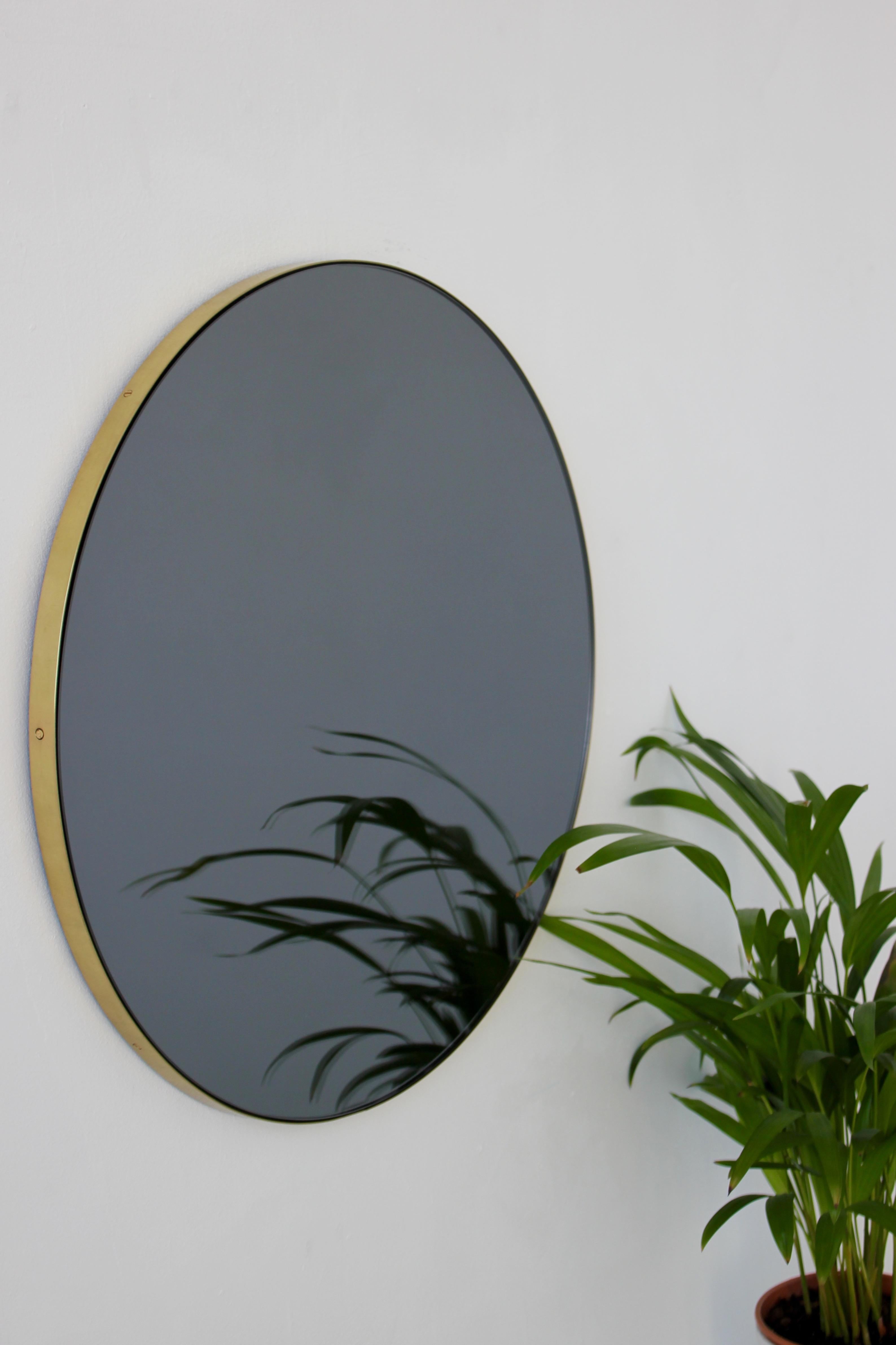 Miroir rond contemporain teinté noir avec un élégant cadre en laiton brossé. Les détails et la finition, y compris les vis en laiton visibles, soulignent l'aspect artisanal et la qualité du miroir, véritable signature de notre marque. Conçu et