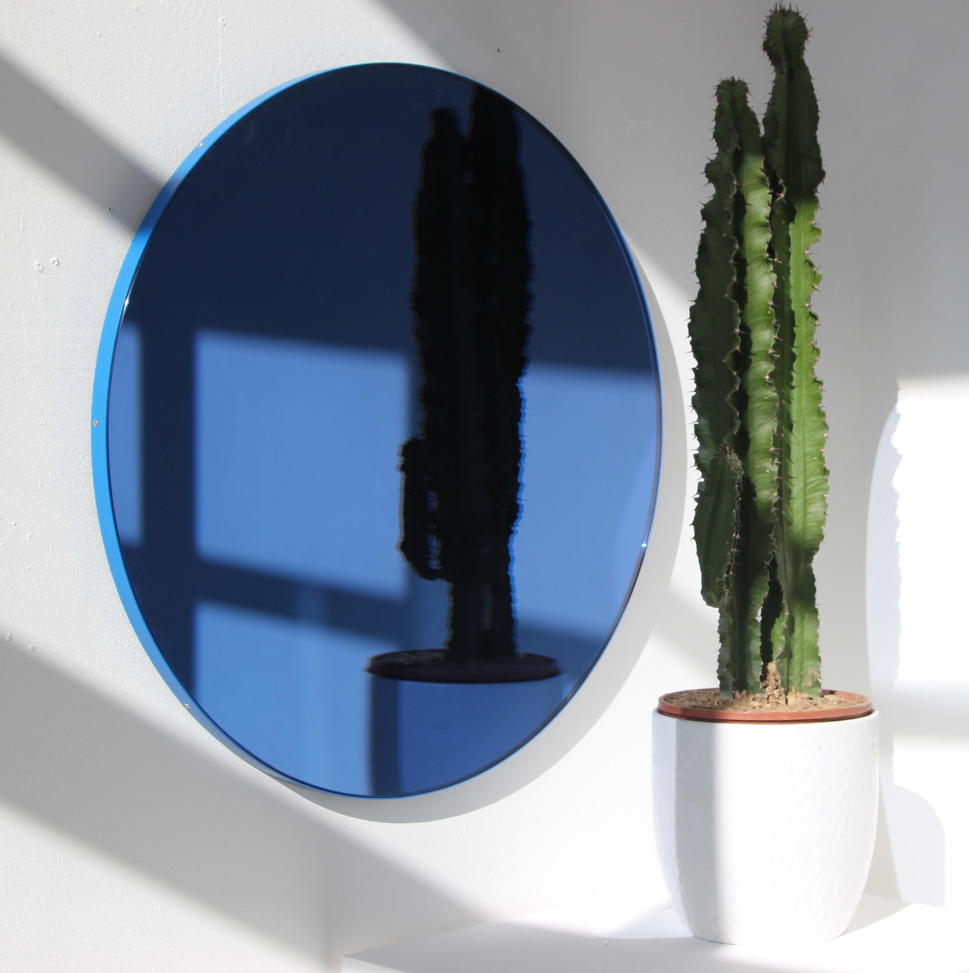 Moderner, blau getönter, runder Spiegel mit einem lebendigen, pulverbeschichteten, blauen Aluminiumrahmen. Entworfen und handgefertigt in London, UK.

Unsere Spiegel sind mit einem integrierten französischen Befestigungssystem (geteilte Leisten)