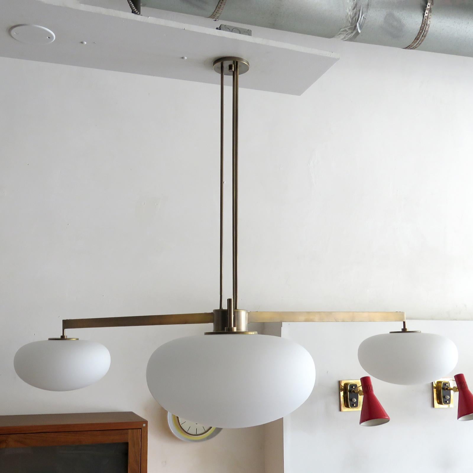 Superbe lustre à trois bras de Gallery L7, fabriqué et fini à la main à Los Angeles en laiton américain avec une finition en laiton vieilli et trois globes en verre opalin mat, mesure 40 x 60 pouces (h x d), la hauteur peut être personnalisée sur