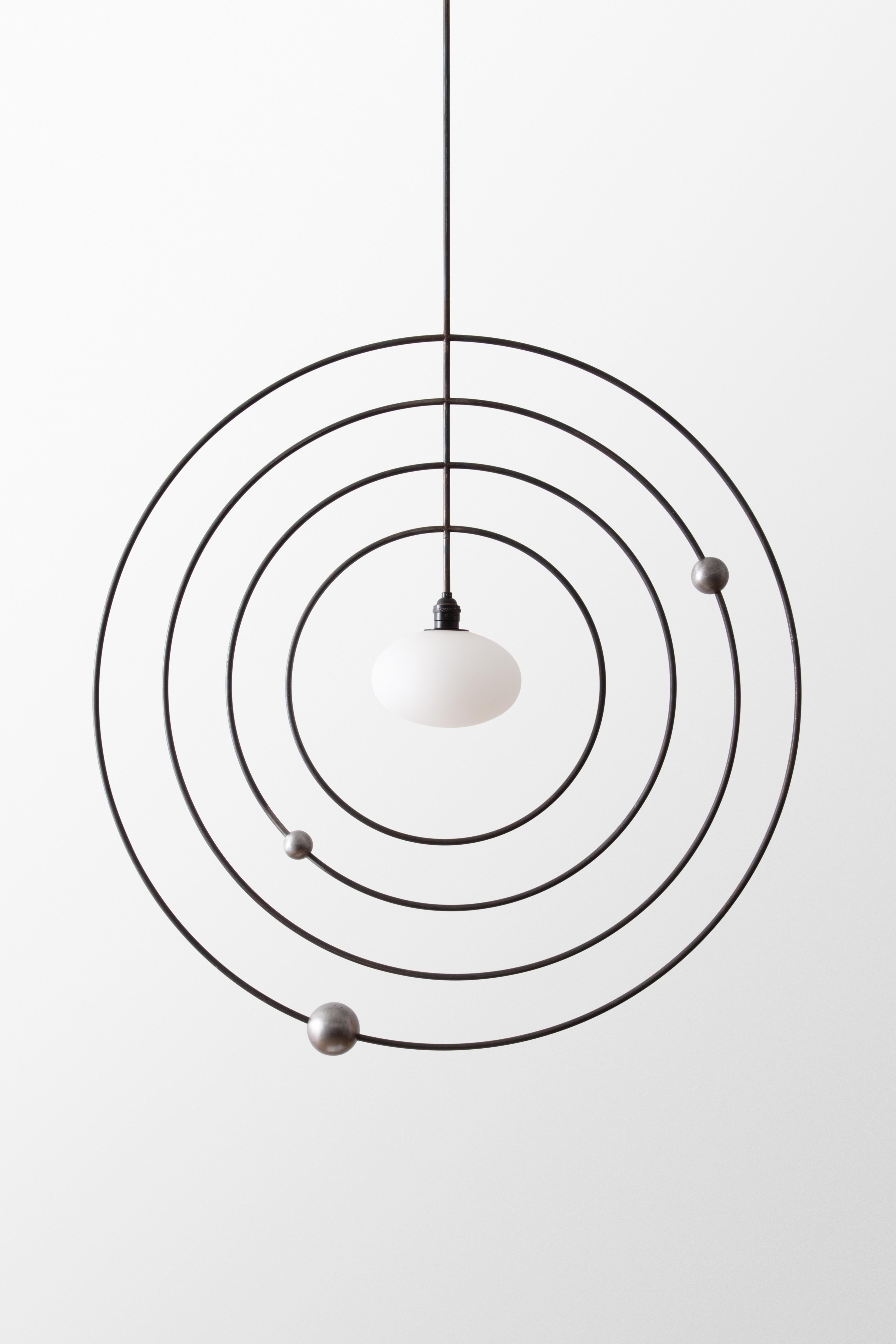 The Mobile series combine sculpture with lighting, invoking motifs from atomic models and the space age. The concentric rings can be spun and reconfigured, inviting play and whimsy. The central orb illuminates the steel rings, which are