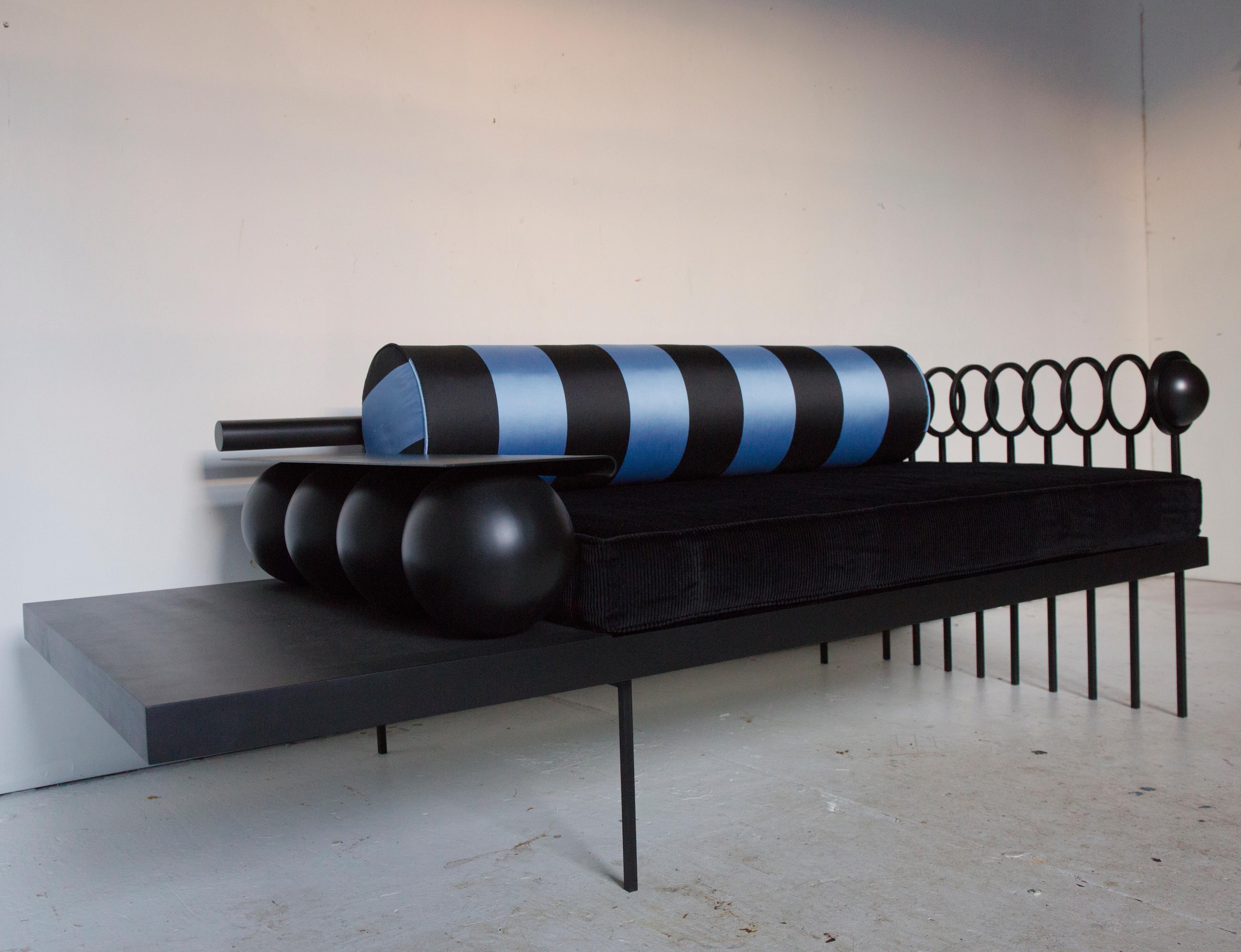 The Orbital Plane Loveseat in matte black lacquered steel is paired with a lush wide wale corduroy cushion and lustrous striped bolster.  The steelwork is evocative of the atomic era, and unifies contemporary design with a playful geometry. 