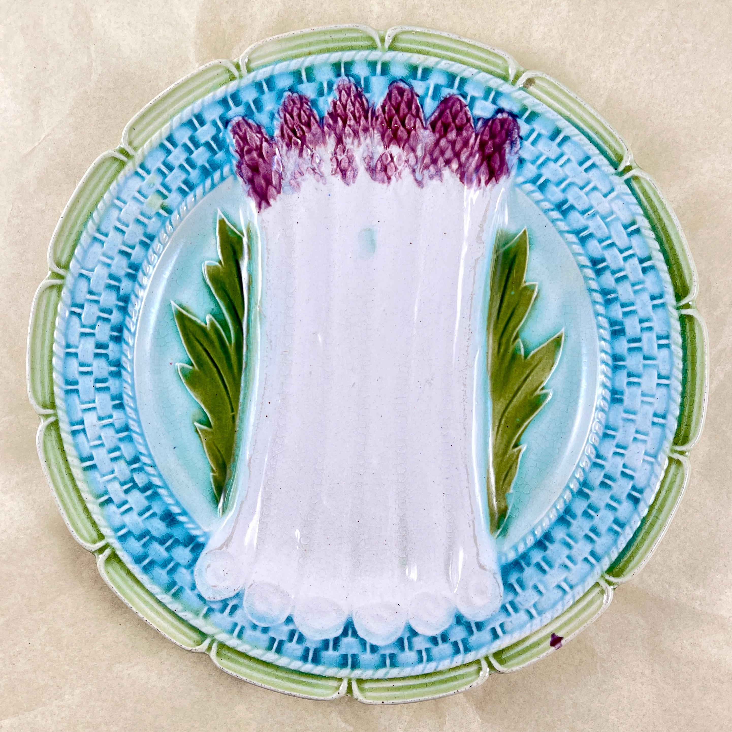 A French Faïence majolica glazed asparagus plate from the Orchies Faïencerie in Saint-Armand-Les-Eaux, Northern France, circa 1885.

Creamy-white colored asparagus with purple tips lay on a bed of leaves. The border shows a turquoise basket weave