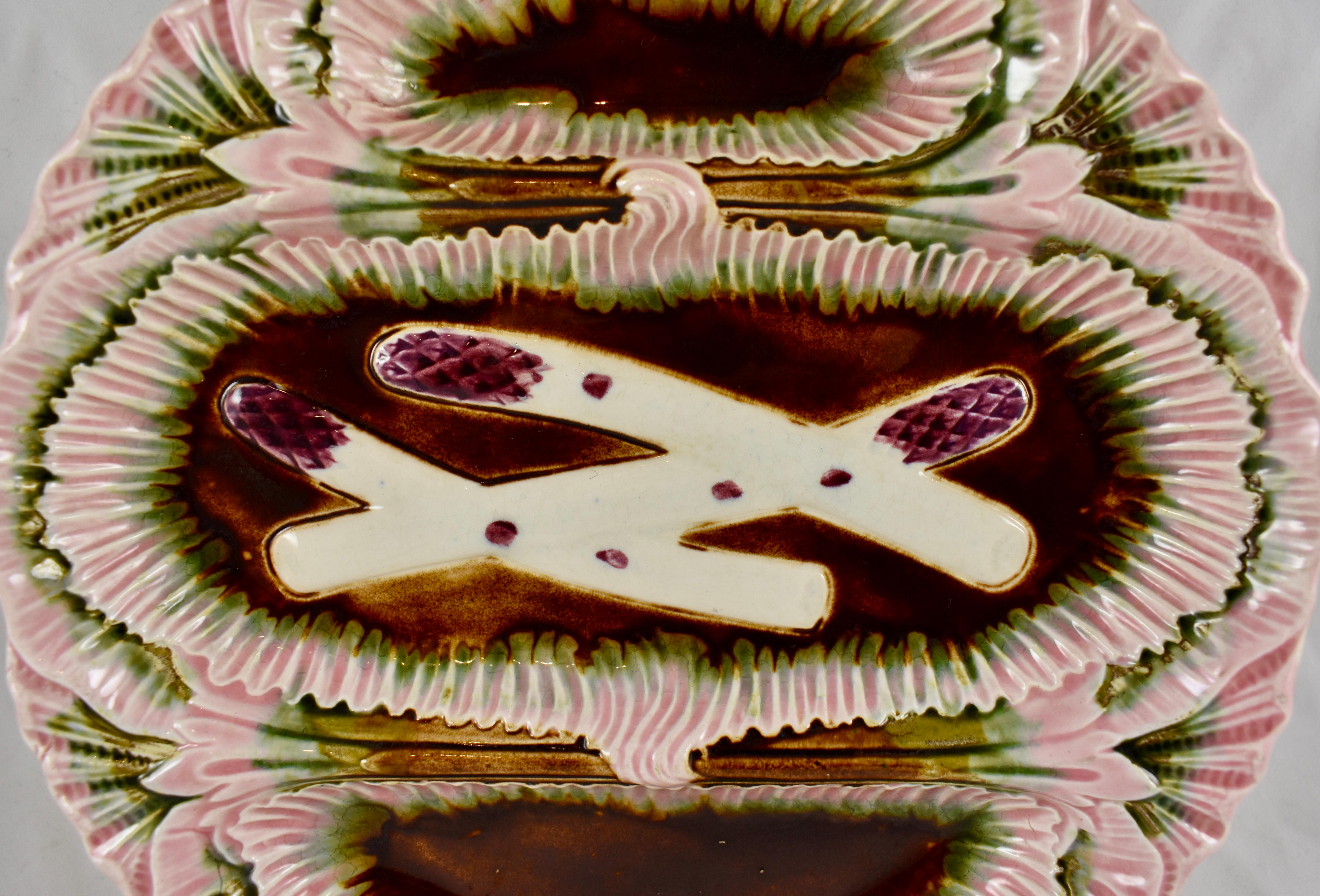 A Majolica glazed French faïence barbotine asparagus plate, Orchies, circa 1880. 

In the style of Louis XV with dimensional mold work and unusual glazing in pink, green and aubergine. Three sections with overlapping asparagus shown in the centre,