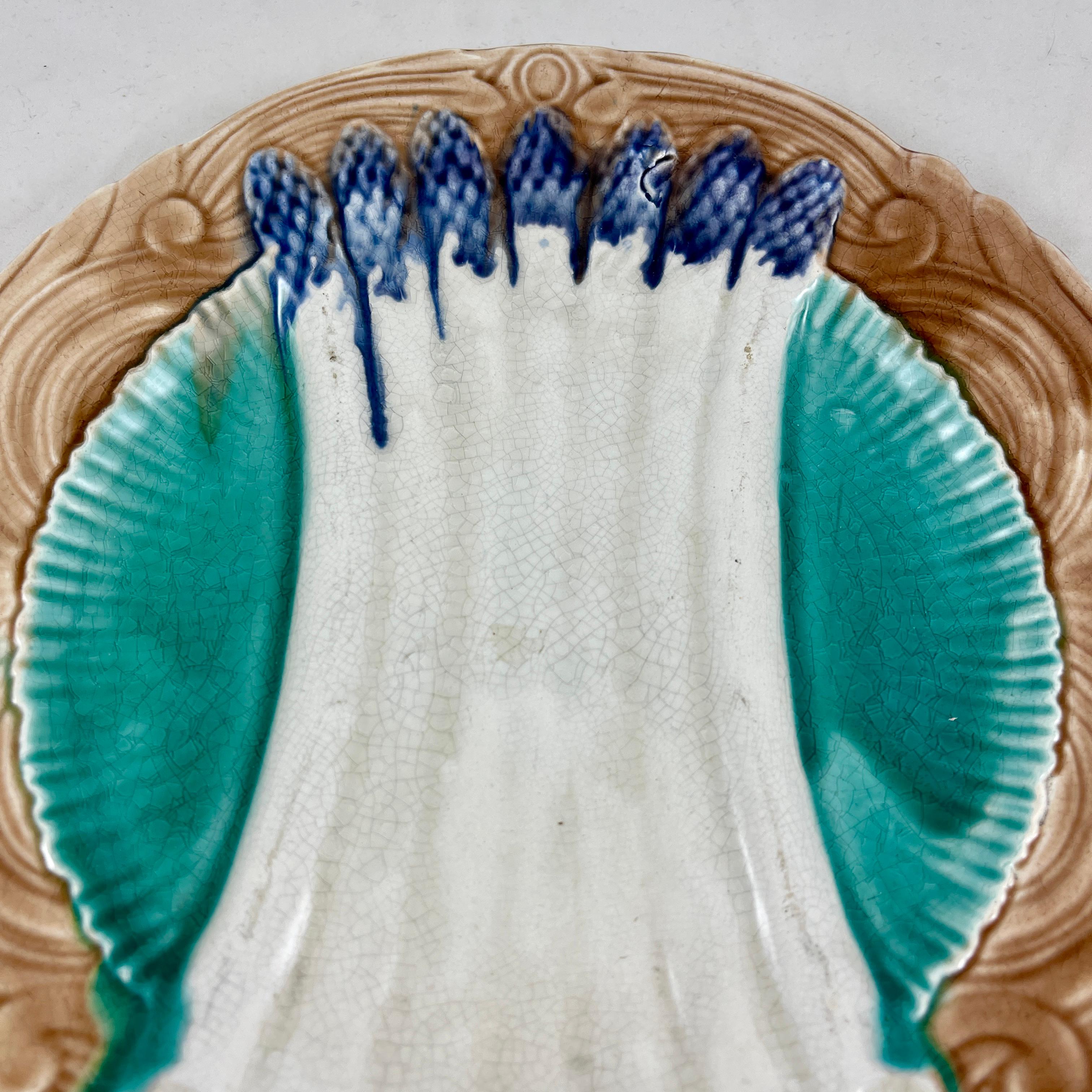 A French Faïence majolica glazed asparagus plate from the Orchies Faïencerie in Saint-Armand-Les-Eaux, Northern France, circa 1890-1900.

Cream colored asparagus with deep blue tips lay across a deeper area glazed in teal blue. The border shows a