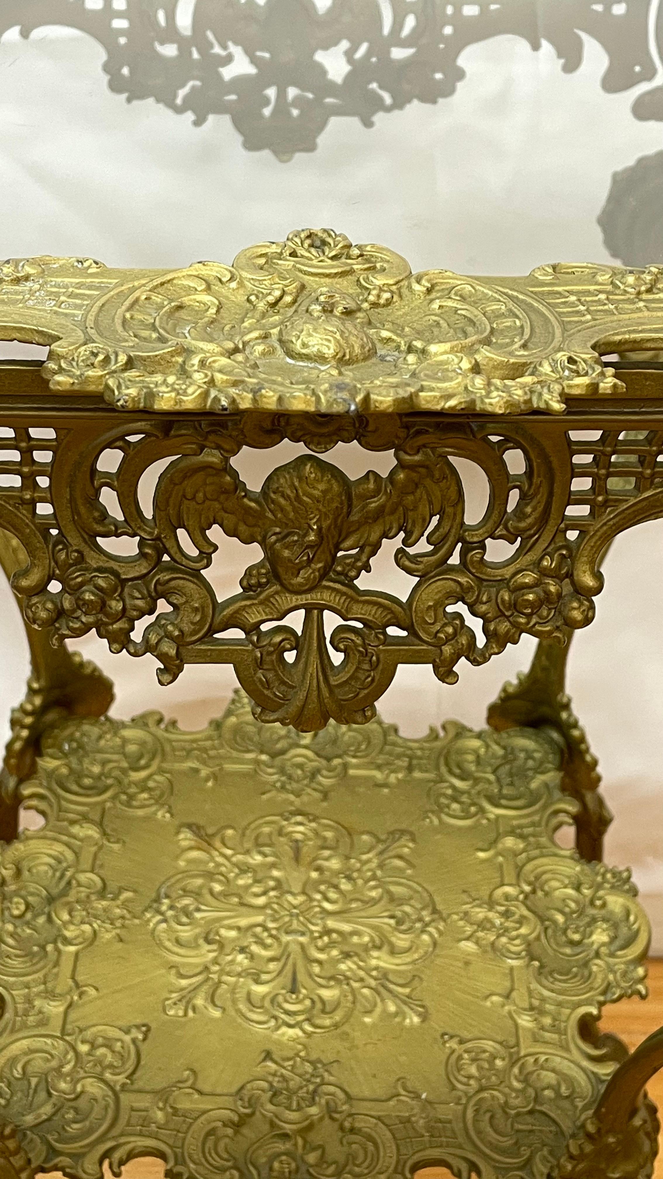 Ornate 1920's Two-Tier Brass Table w/Glass Top decorated with cherubs  In Good Condition For Sale In San Francisco, CA