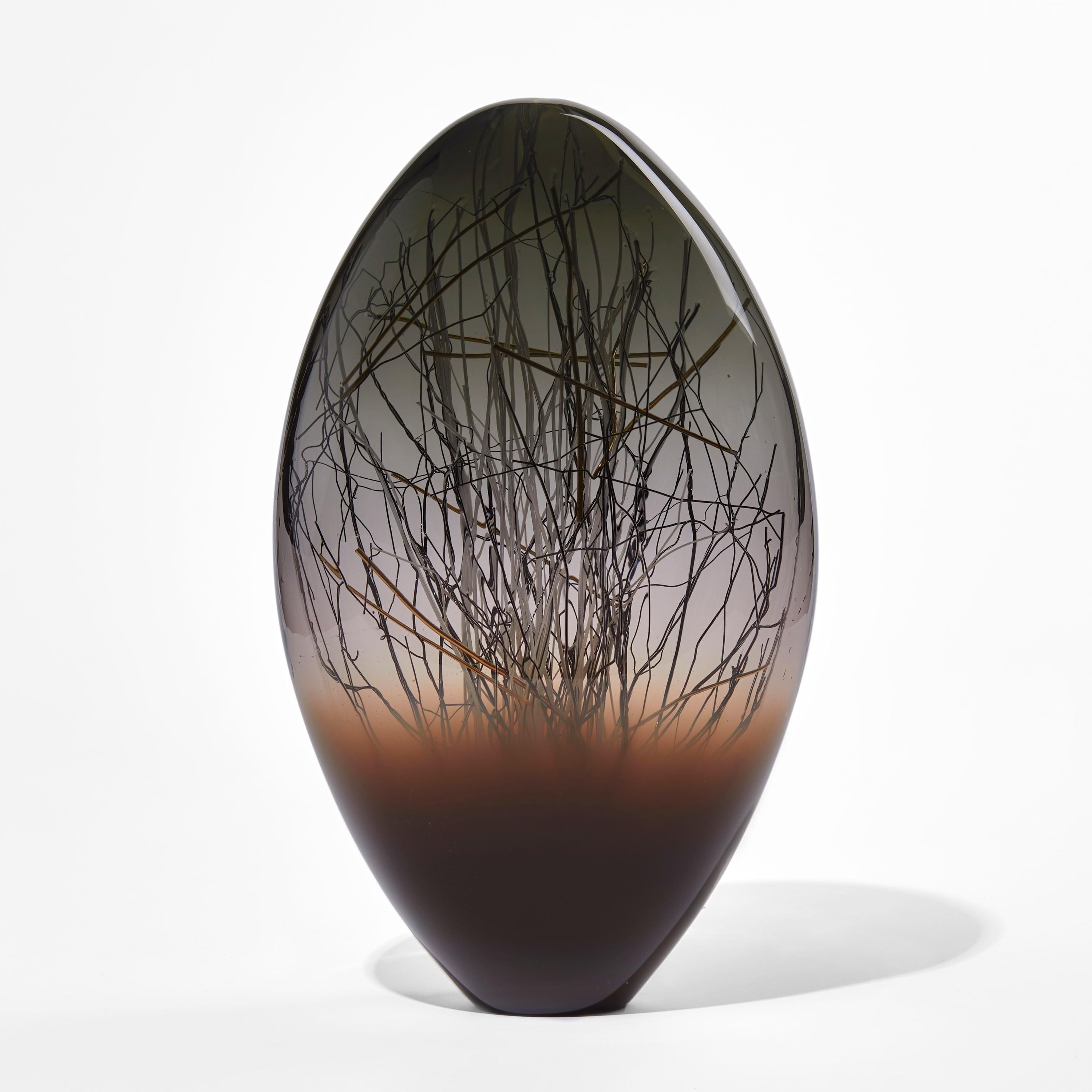 Ore Eclipse in Coffee & Grey is a unique glass sculpture in dark grey, rich brown, black and clear colored glass by the collaborative artists Hanne Enemark (Danish) and Louis Thompson (British). The outer glass form contains a multitude of fine
