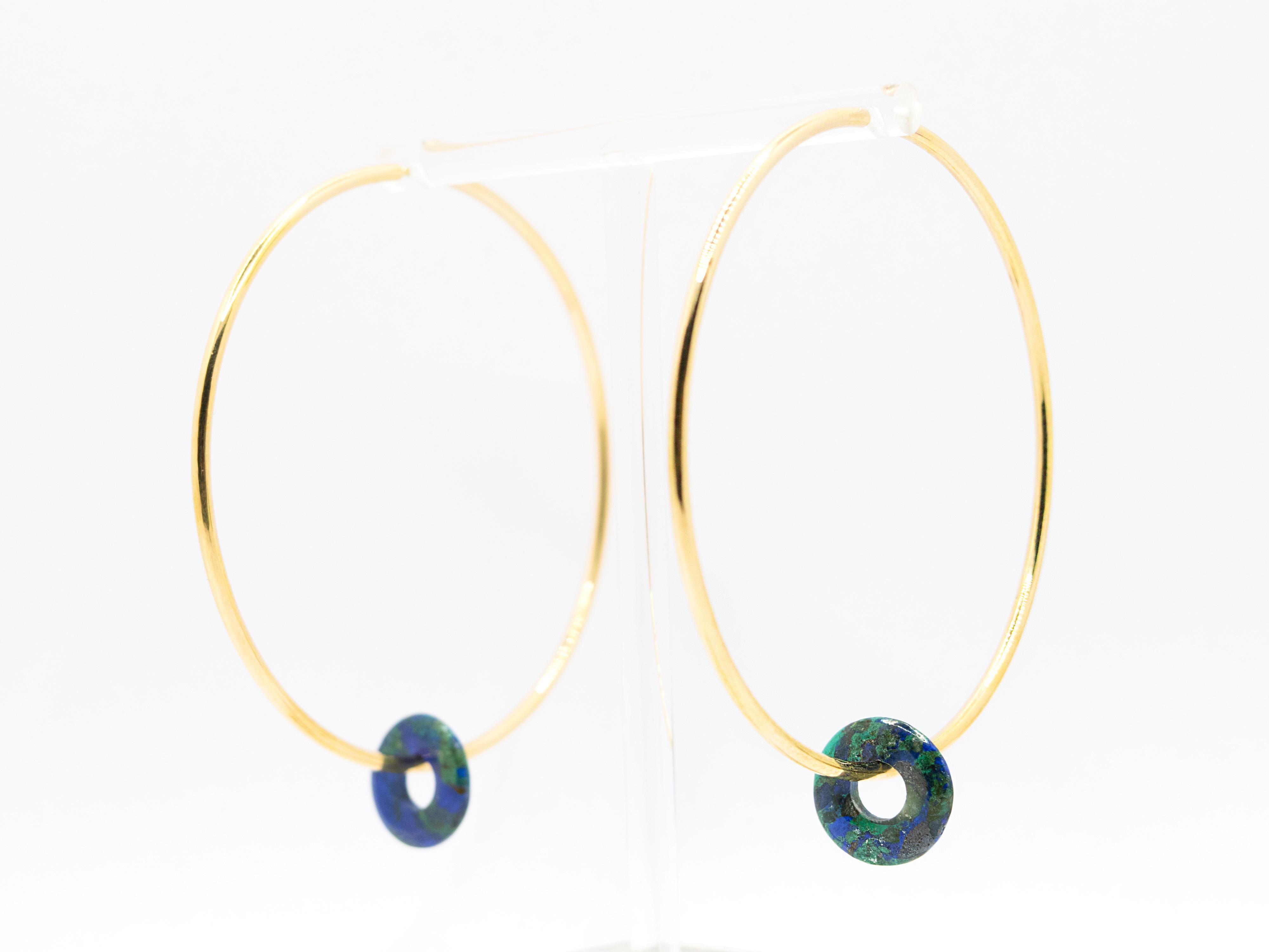 A cute pair of hoop earrings with a diameter of 7 cm ( 2.75 in ). 
These earrings are made of 18kt gold  weighing 9.15 g .
They are lightweight and wearable all day long.
Enriching the design is a movable Azurite ( variety of Malachite ) disc, so