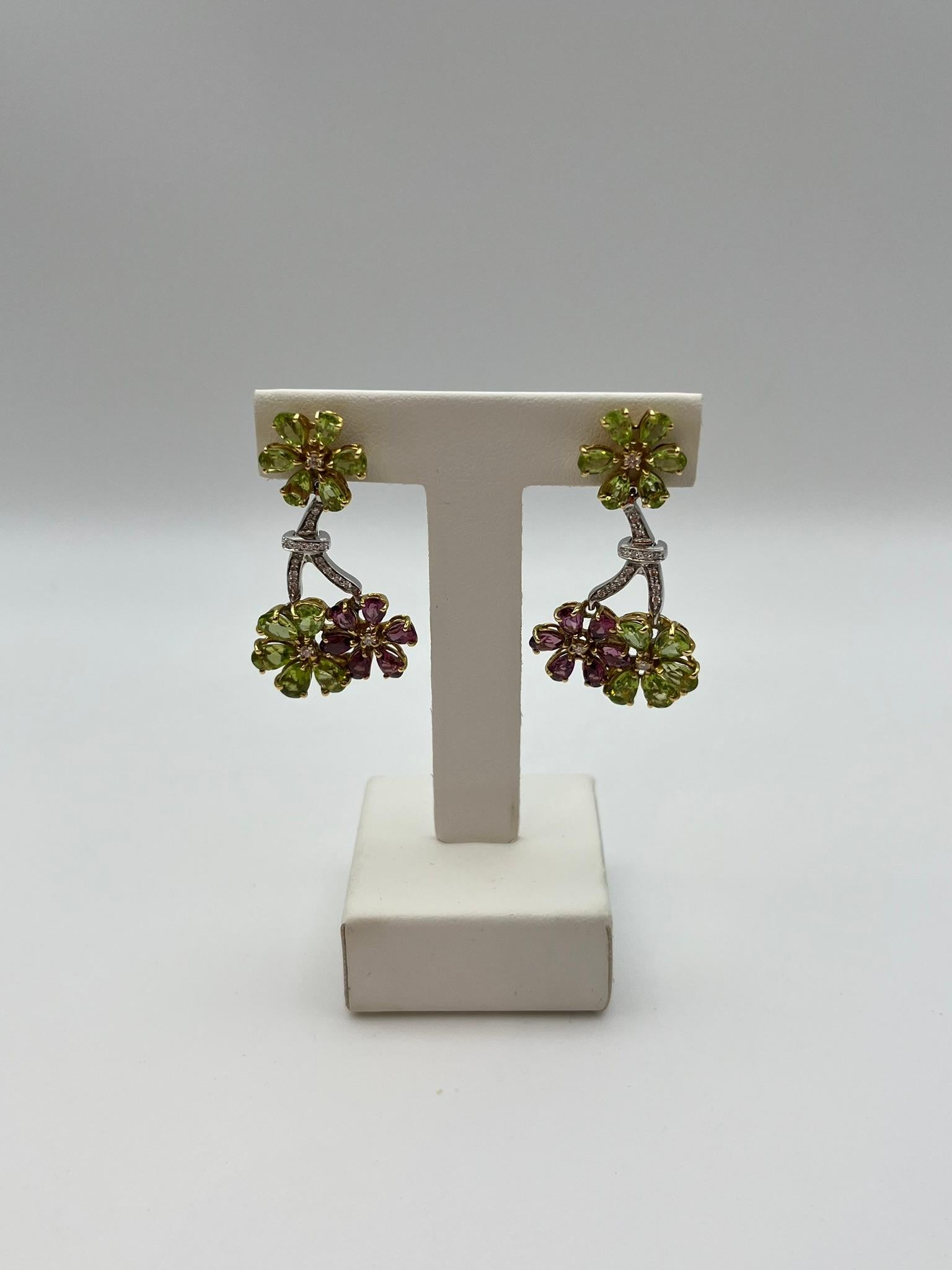 Raffinati orecchini realizzati artigianalmente in Italia in oro bianco e giallo 18 kt. 750/00. La composizione floreale è ondulata, un dettaglio che li impreziosisce e caratterizza. Ogni fiore è composto da un'alternanza di peridot e rodolite
