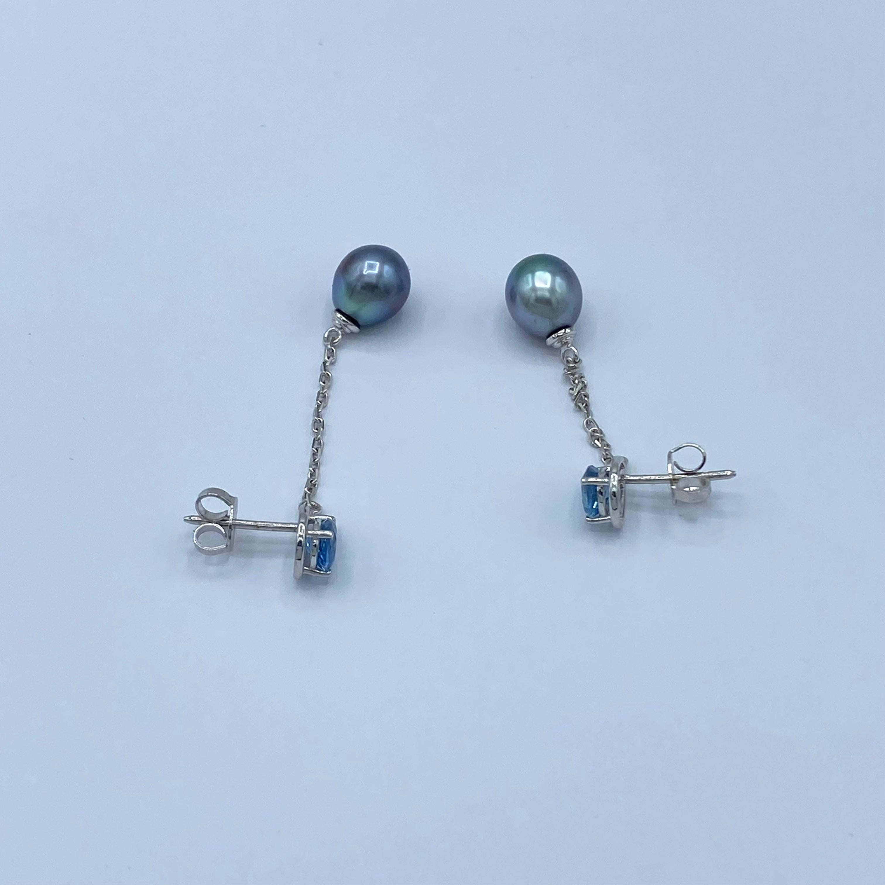 Questi raffinati orecchini in oro bianco 18Kt nascono dall’incontro armonioso tra due perle di Tahiti ovali da circa 8,5 mm, dalle delicate sfumature grigio-azzurre, e due eleganti gocce di acquamarina da 5x7 mm, per un totale di 1,11 carati.
Il