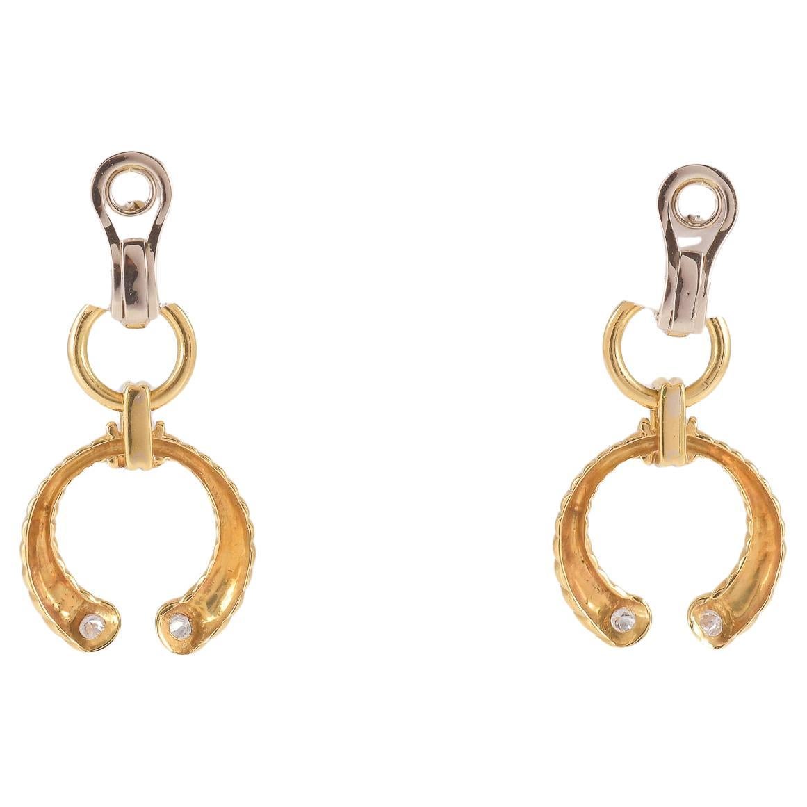 Paire de boucles d'oreilles en or jaune 18 carats (750/1000) marquées '750 83PV', chacune constituée d'un clip auquel est suspendu un pendentif en or clouté et décoré de petits diamants.
Le poids de l'objet est de 18,87 grammes.
Une description