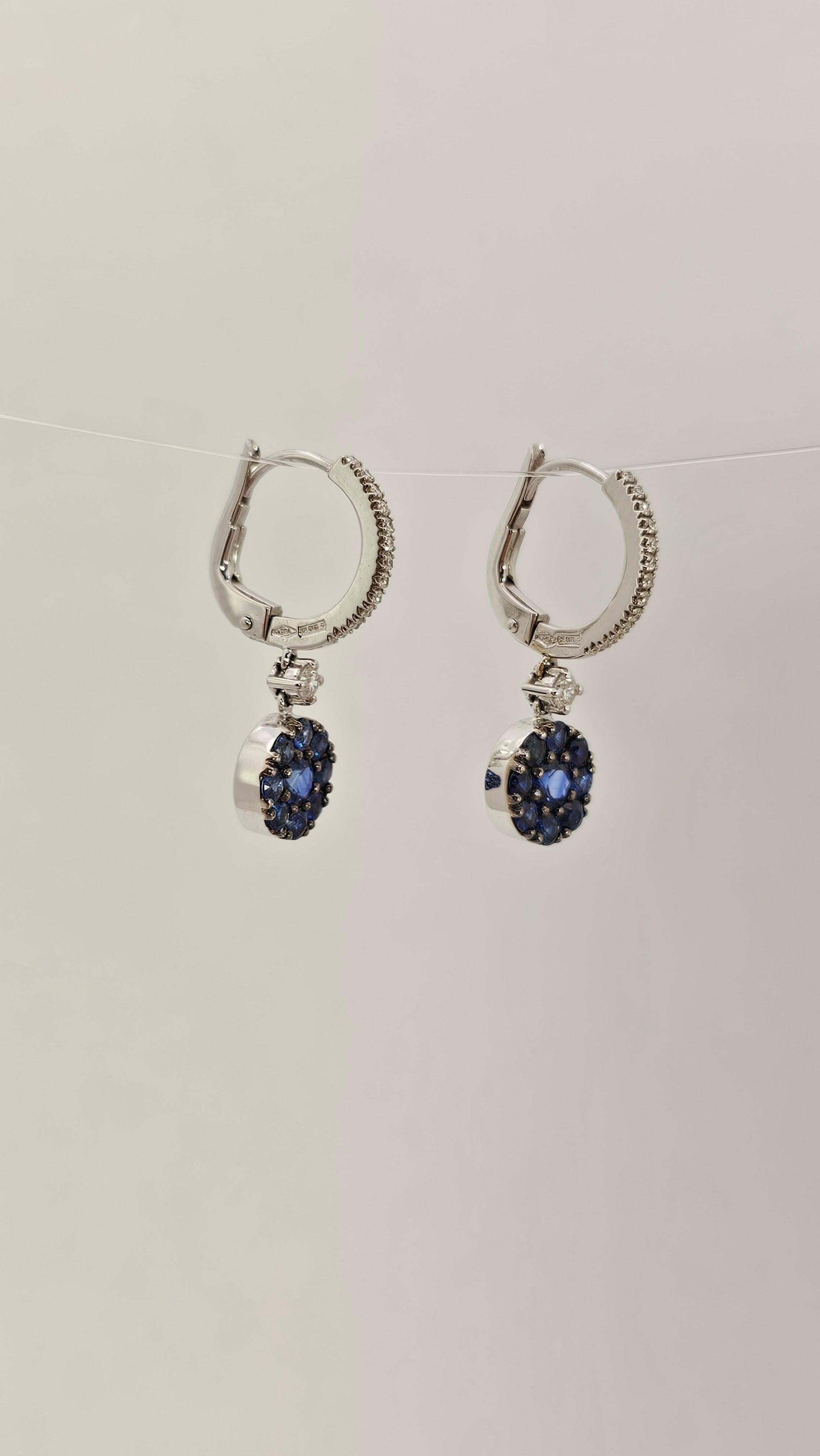 Gorgeous pair of 18kt white gold, Diamonds and Blue Sapphires dangle earrings.

This model is made by a hoop top with Diamonds and lever closure.
The dangling part of the earring is composed of a round white gold tablet, embellished with multiple