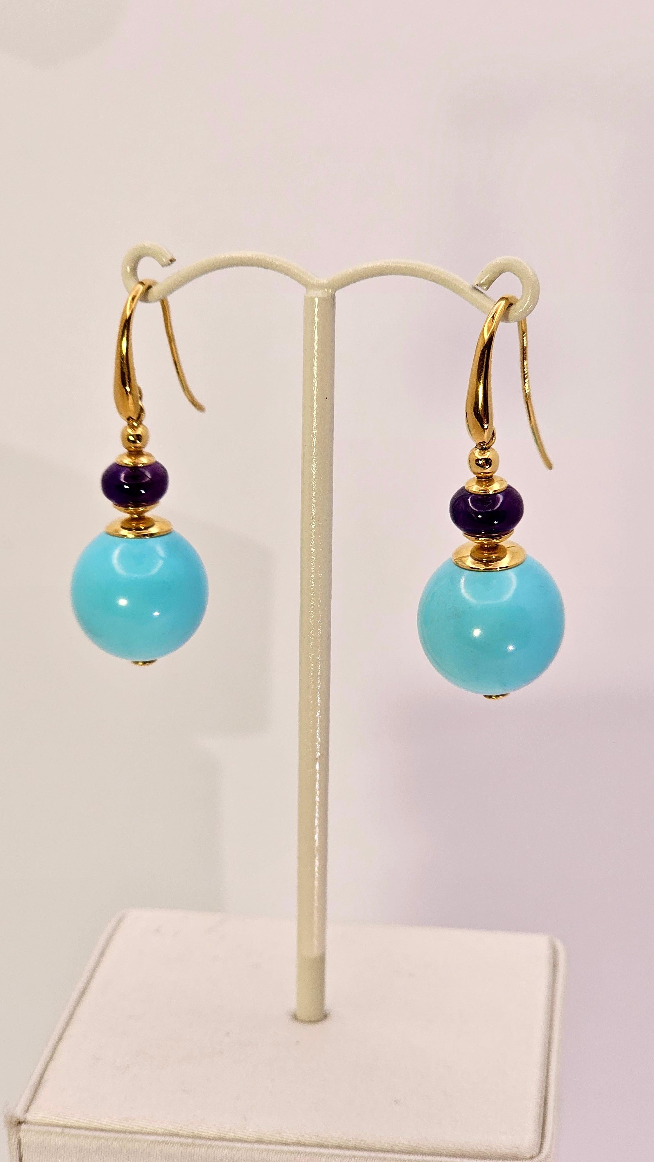 Un paio di orecchini pendenti dal design anni '60, realizzati a mano da maestri artigiani orafi, caratterizzati da uno splendido ed originale abbinamento di colori, turchese e viola.
Diese Schmuckstücke sind aus 18-karätigem Gold mit einer