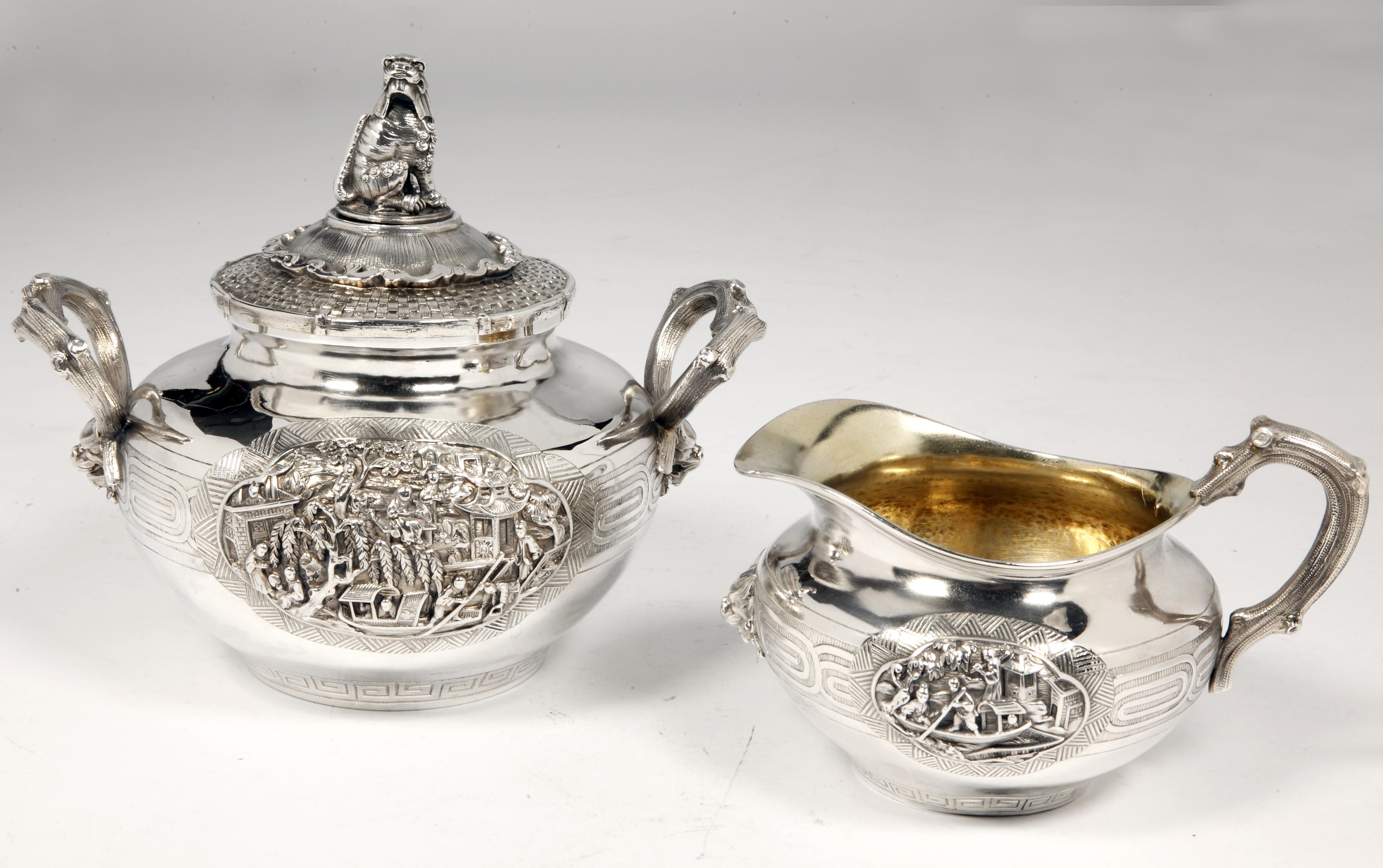 These pieces are made of solid silver. The body is plain, on a flat background, decorated with a Greek frieze and applied on both sides, village scenes in Chinese style. The lid of the sugar bowl is beautifully carved with a woven wicker imitation