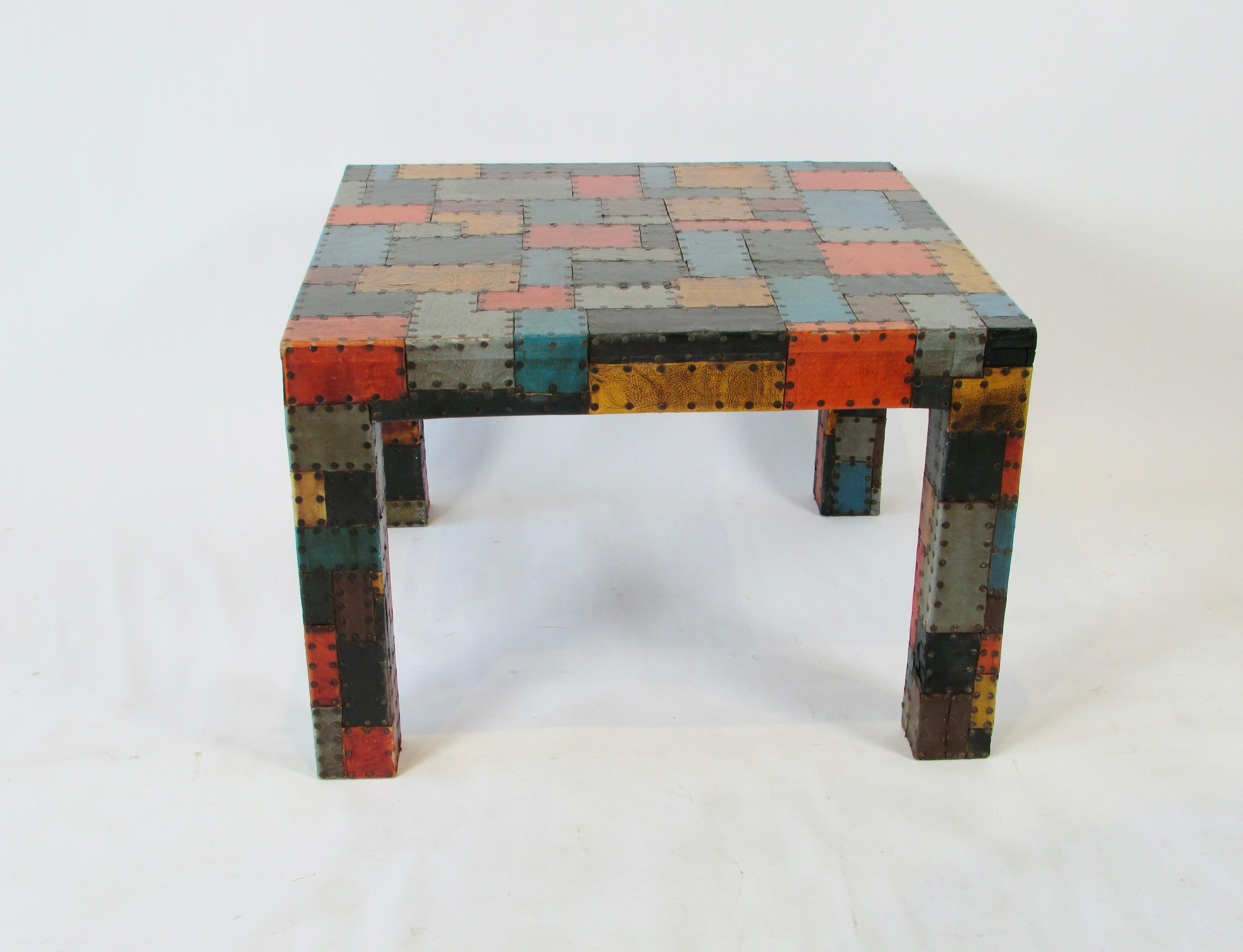 Nicely executed folk art parsons style table. Covered in leather square patches of varying size and color in geometric design. Fine scale and nicely matched colors. Each piece hammered to wooden table structure.