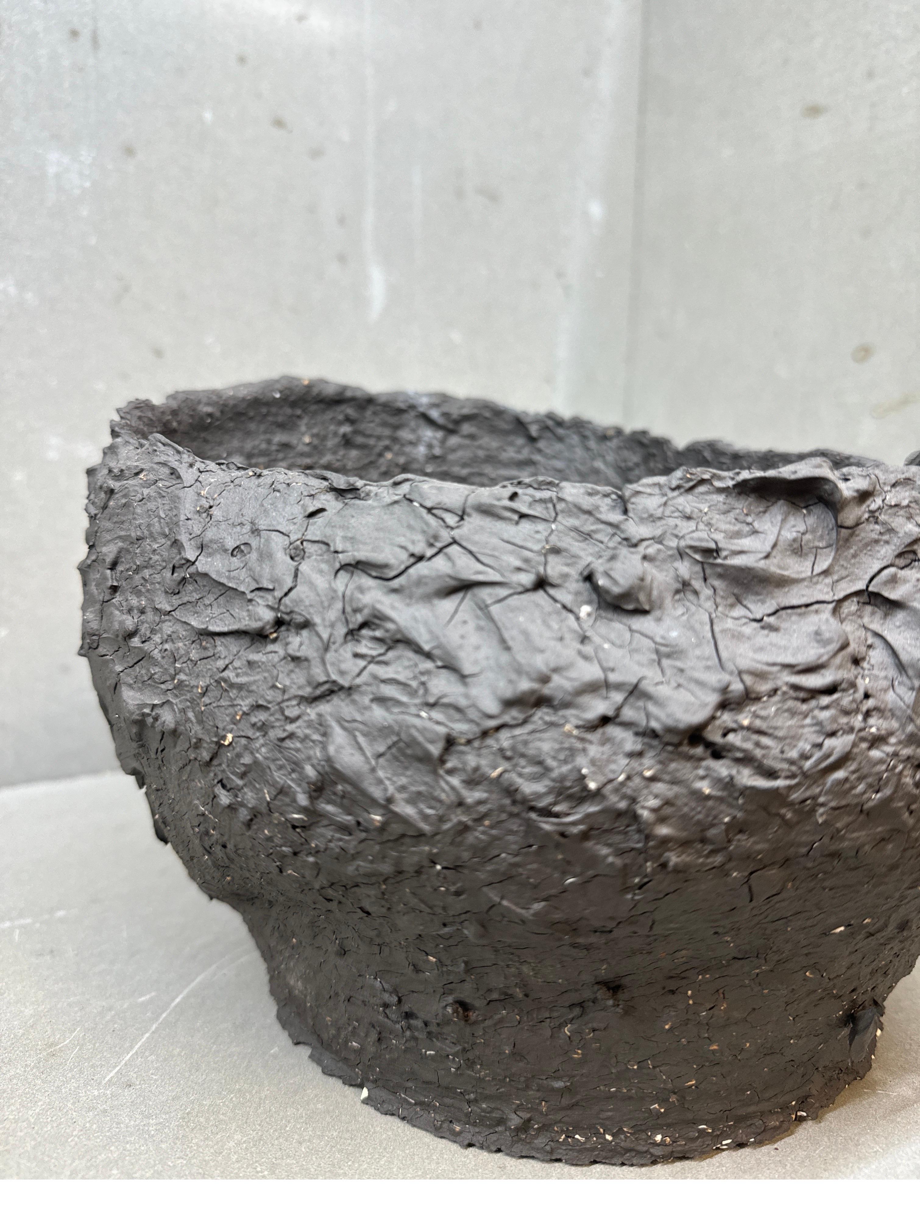 Este recipiente escultórico de cerámica surge como un fragmento de la propia tierra: su superficie dentada y craterizada recuerda antiguas formaciones de lava o la piel agrietada de un árbol carbonizado. Hecha a mano mediante procesos de bajo