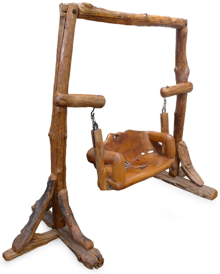 An incredible, organic wood swing. A combination of carved-wood and cut-branch components; a slight, two-seat bench suspended from an aesthetically-primitive yet thoughtfully-constructed overhanging frame. A wonderfully gnarled, naturally textured