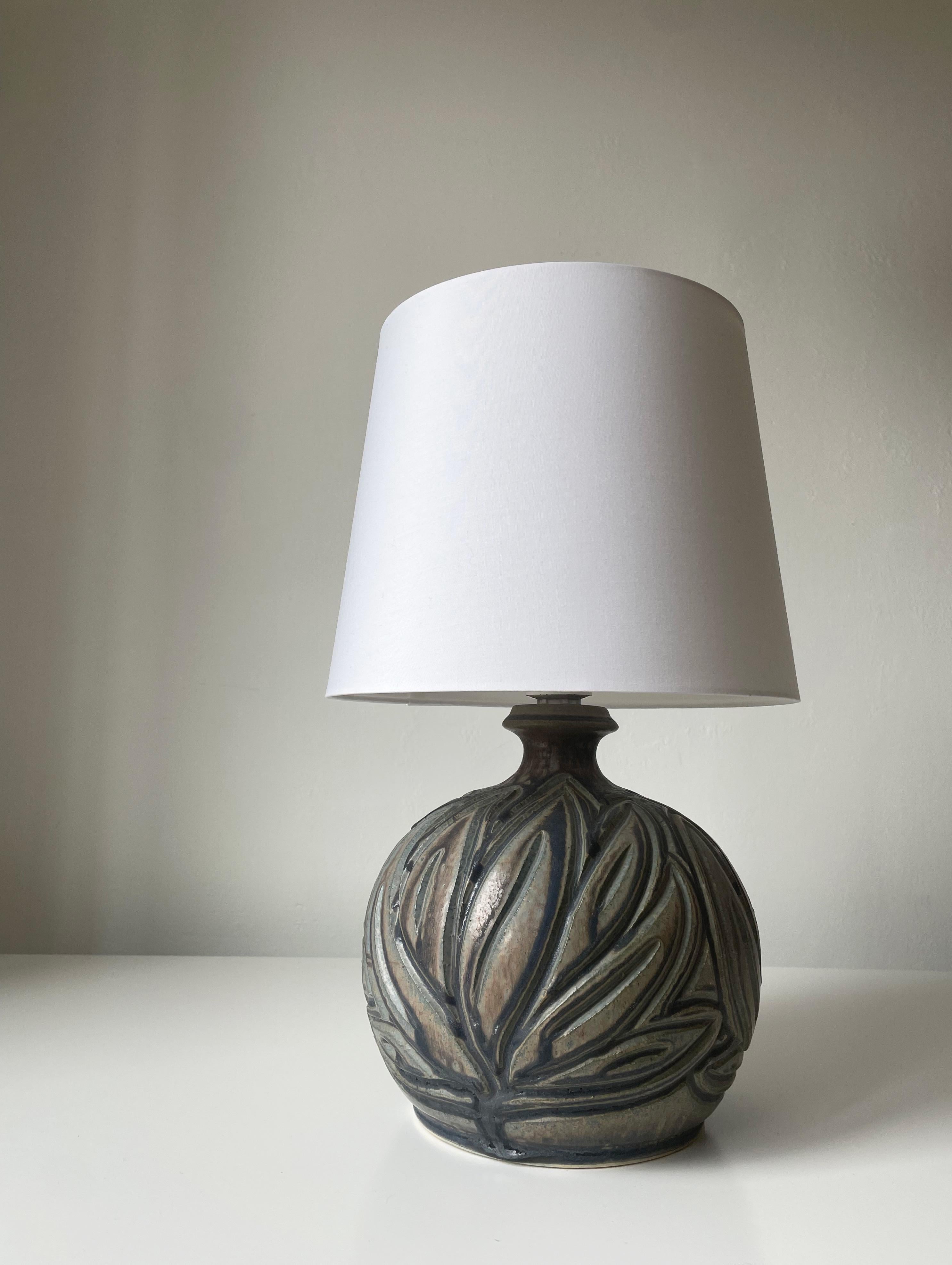 Soft shaped Scandinavian modern stoneware table lamp with large organic leaf like incised relief decorations glazed beautifully in shades of gray, brown, blue, green and anthracite with a slight sheen. Short slender neck with collar. Manufactured in