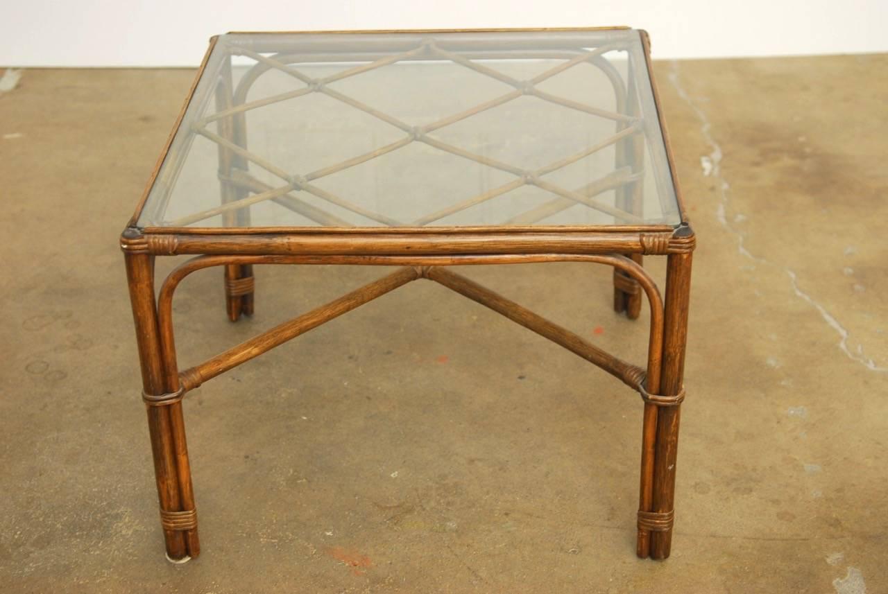 Organic modern coffee table or cocktail table by Brown Jordan constructed from bamboo and rattan. Featuring a decorative open fretwork design lattice top covered with a pane of glass. Supported by four legs conjoined with an X-form stretcher. Made