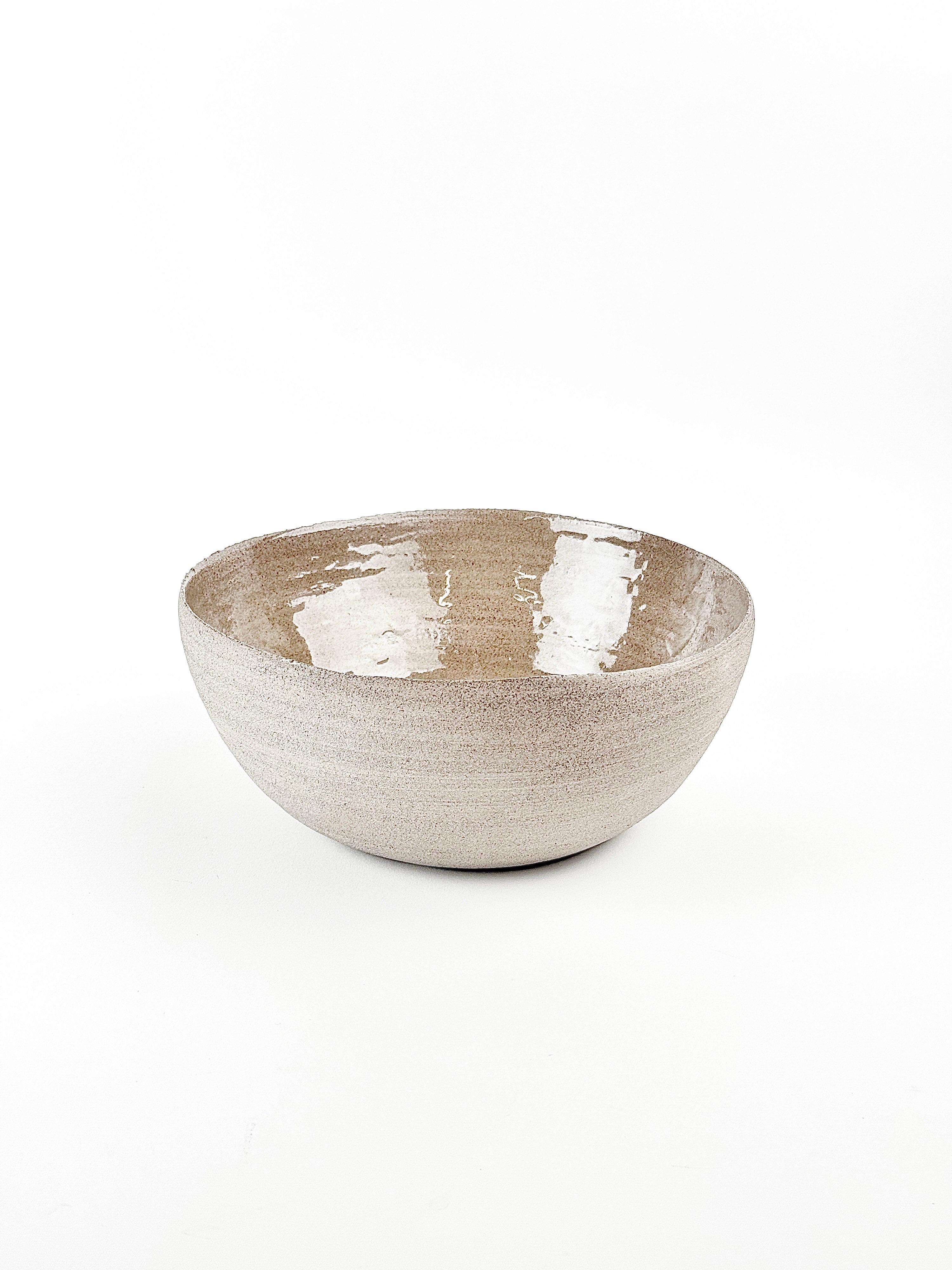 Este cuenco de cerámica, único en su especie y hecho a mano, está elaborado con gres ligeramente moteado, acabado con un suave vidriado interior que realza su tono cálido y natural. Su forma limpia y redondeada y los mínimos detalles de su
