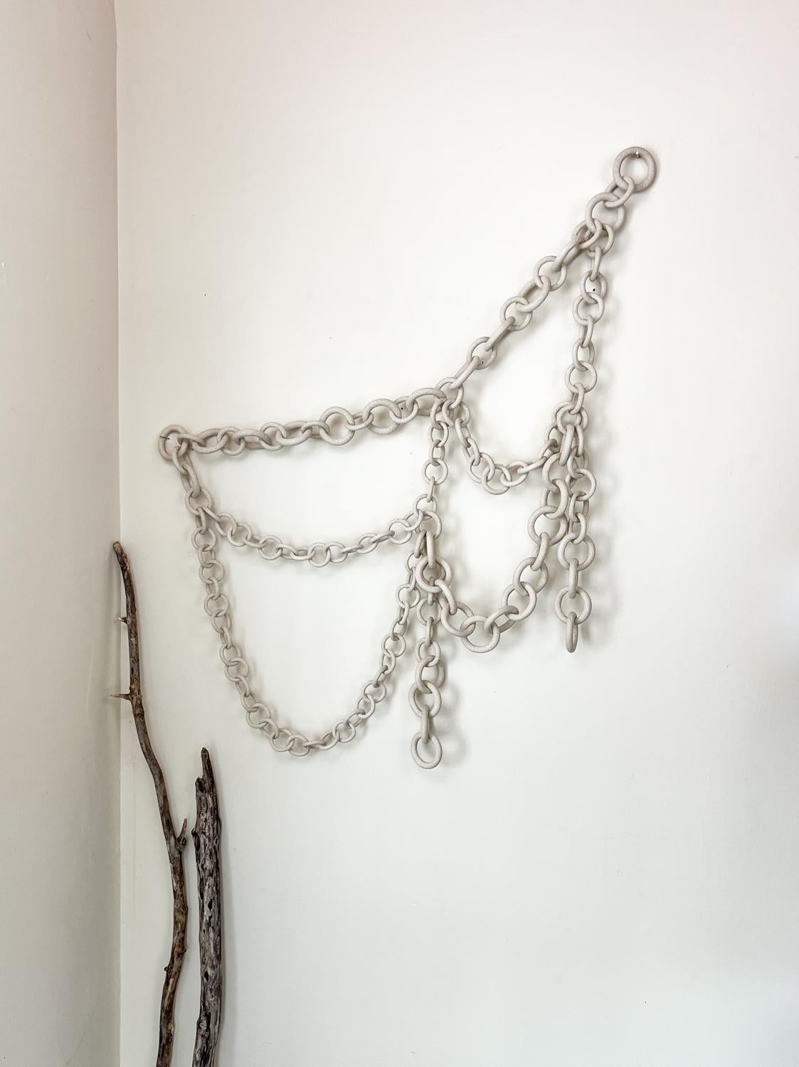 This Ceramic Chain wall sculpture is a unique and captivating piece of art that adds a touch of elegance and intrigue to any space. The sculpture is meticulously crafted by the Artist who skillfully shapes and connects individual ceramic links to