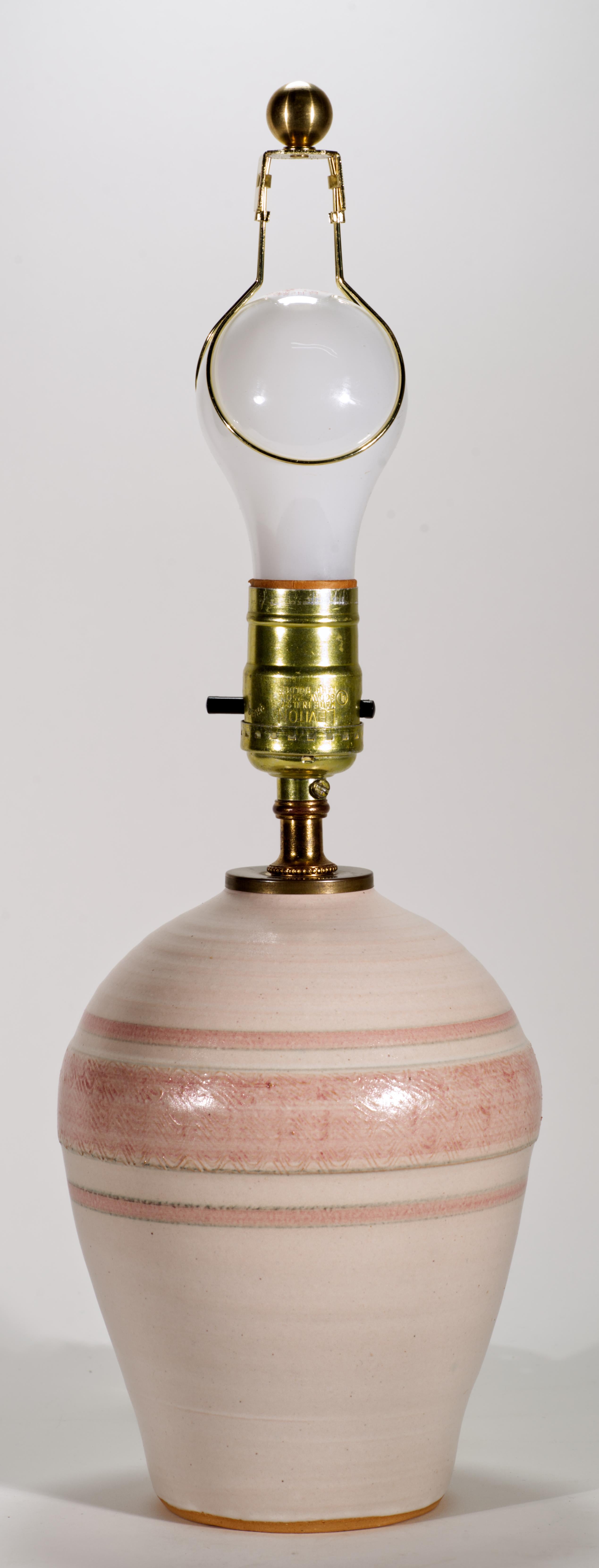  Cette lampe de table ou d'appoint en céramique de studio vintage est décorée d'une bande texturée en relief sur la partie la plus large du corps ; la bande texturée est accentuée par un lavis de glaçure rose clair et de minces bordures roses unies