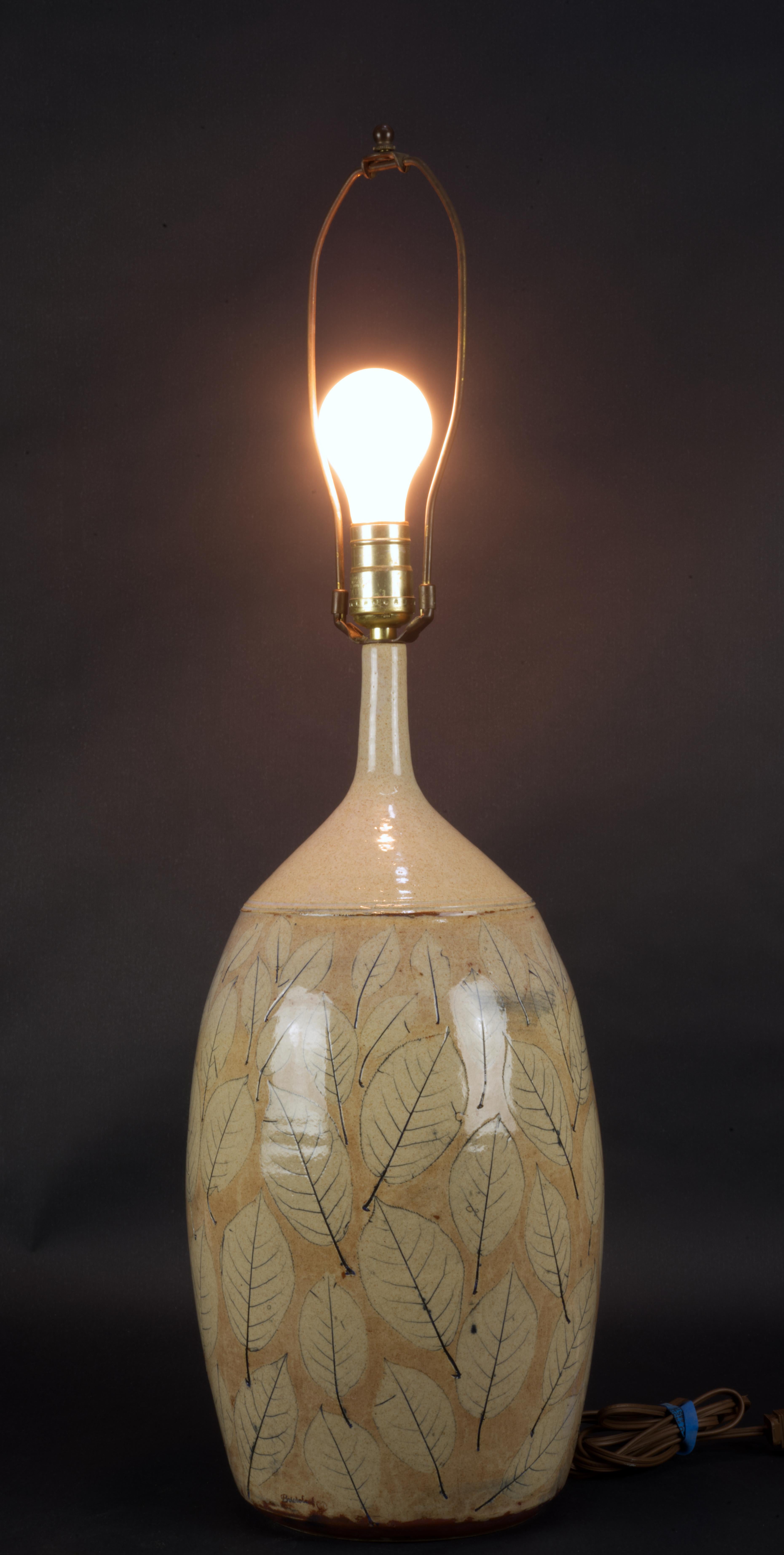  The vintage studio art pottery ceramic table or accent lamp is decorated with hand painted cream and black leaves design on beige background, with top part of the lamp left undecorated in mottled cream glaze. The body of the lamp was hand thrown on