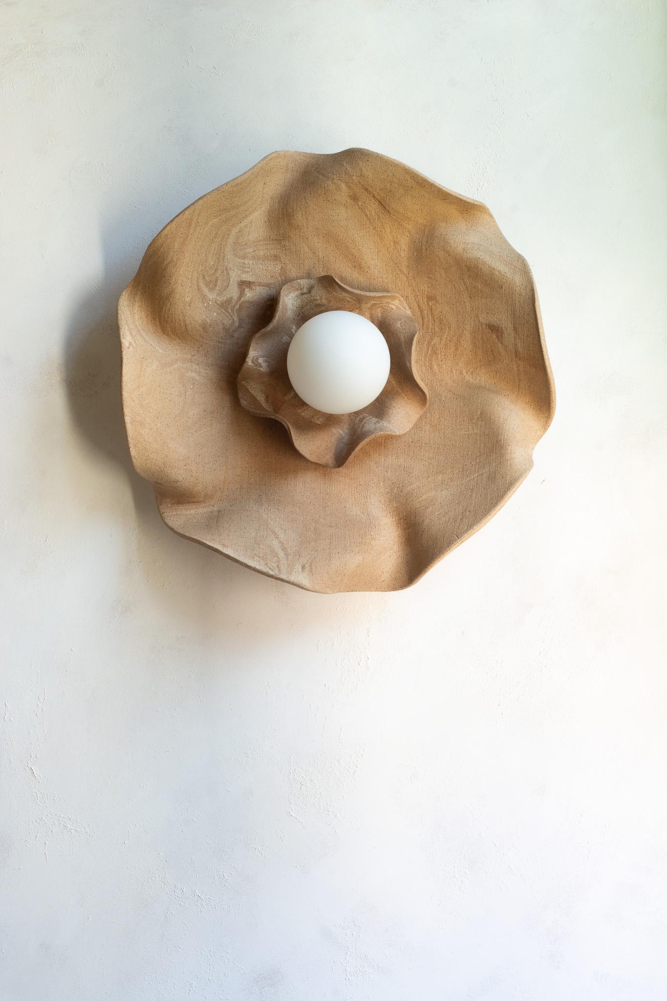 Funcional y escultural a la vez, este aplique de pared presenta un cautivador diseño orgánico y terroso. Se asemeja a una flor floreciente, pero también recuerda a las formaciones geológicas de las montañas.
Esculpida a mano a partir de múltiples