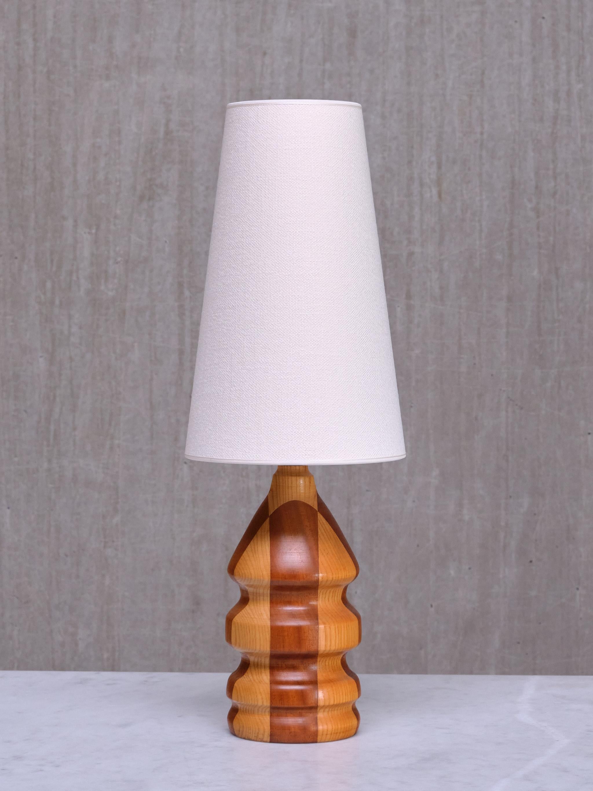 This exceptionally crafted table lamp was produced in Denmark in the 1960s. 

The design features a turned wood base, showcasing a sculptural, curved form with layered tiers that create an abstract bottle silhouette. Another striking effect is