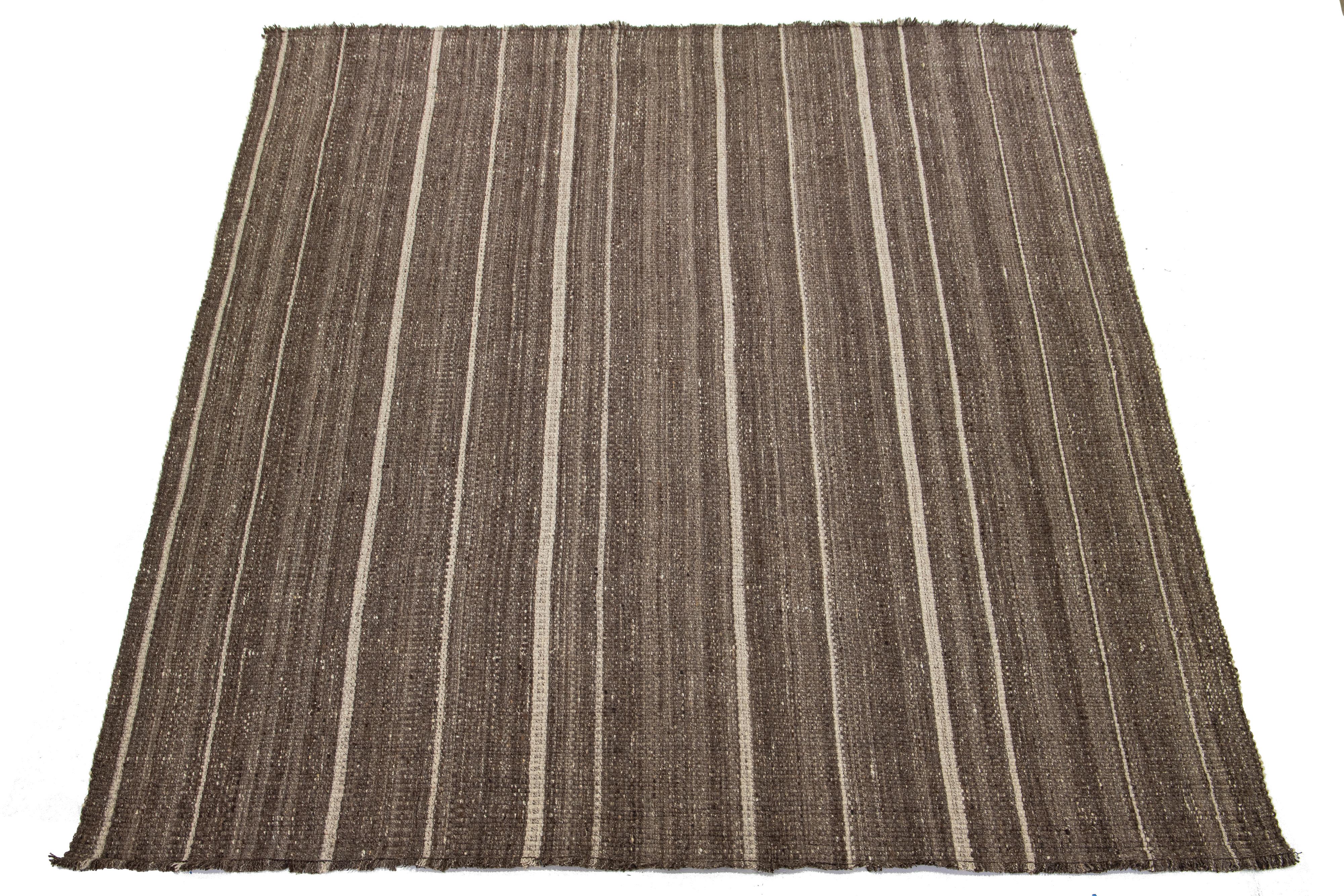 This rug features an organic Apadana's modern wool Kilim flatweave with a striped beige design and a brown base pattern.

This rug measures 12'2